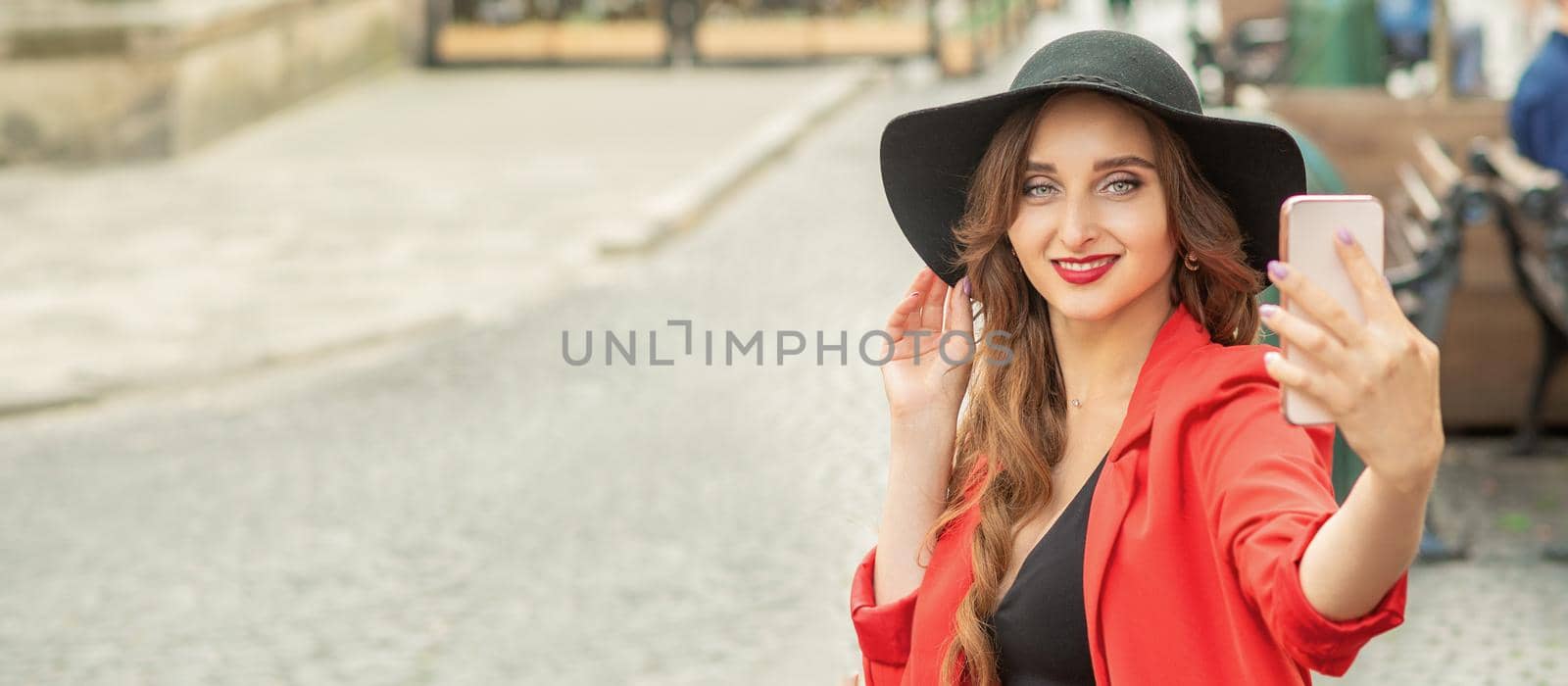 Stylish young woman is taking selfie walking on the street of old European city.