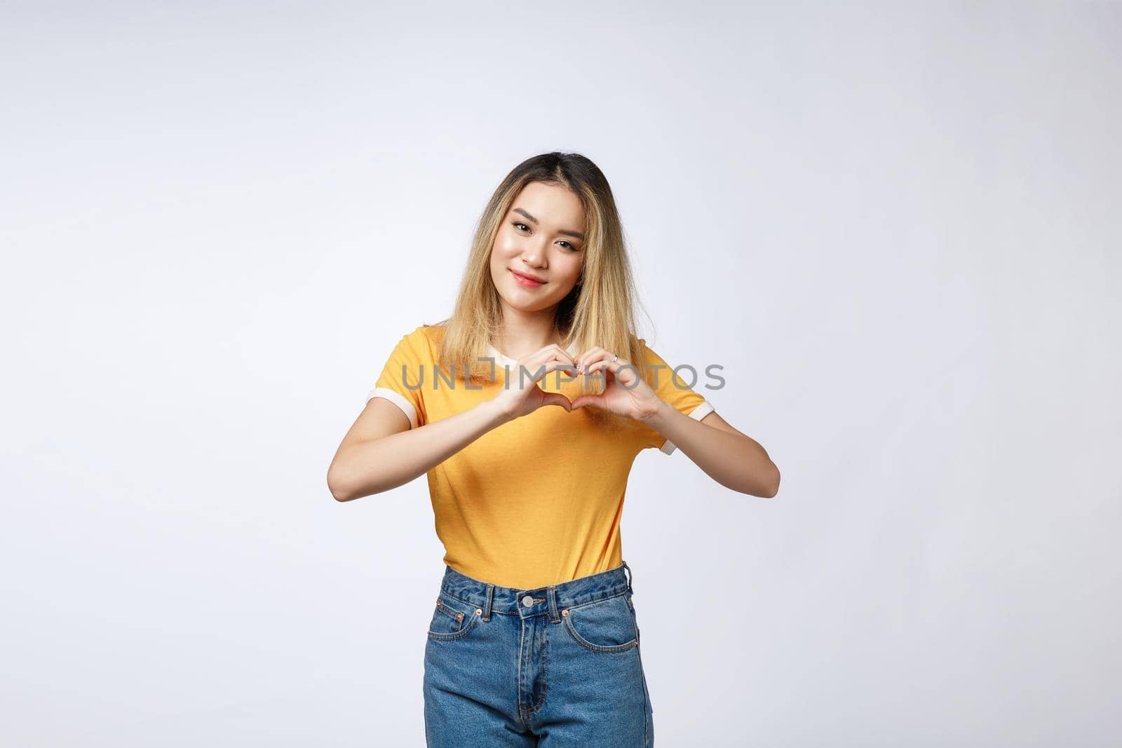 Pretty young asian woman making a heart gesture with her fingers in front of her chest by Benzoix