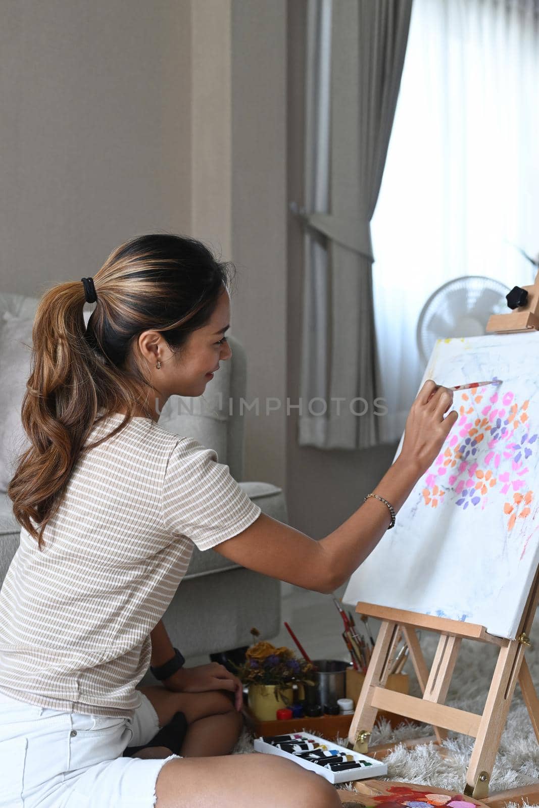 Side view young woman painting picture on canvas with watercolor.