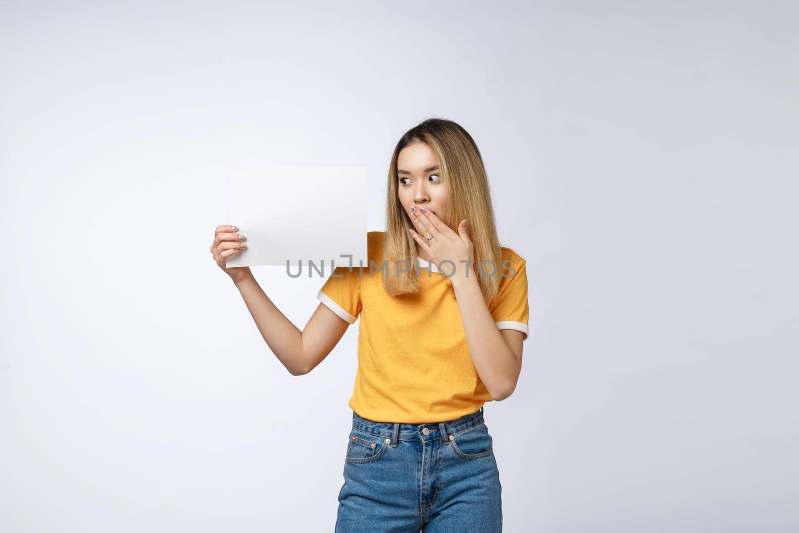 Banner sign woman peeking over edge of blank empty paper billboard with copy space for text. Beautiful Asian Caucasian woman looking surprised and scared - funny. Isolated on white background by Benzoix