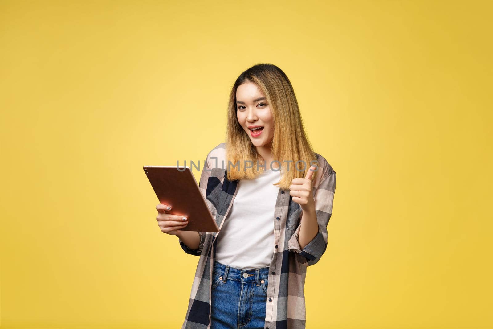 Asian woman use of tablet pc and thumb up isolate on yello background
