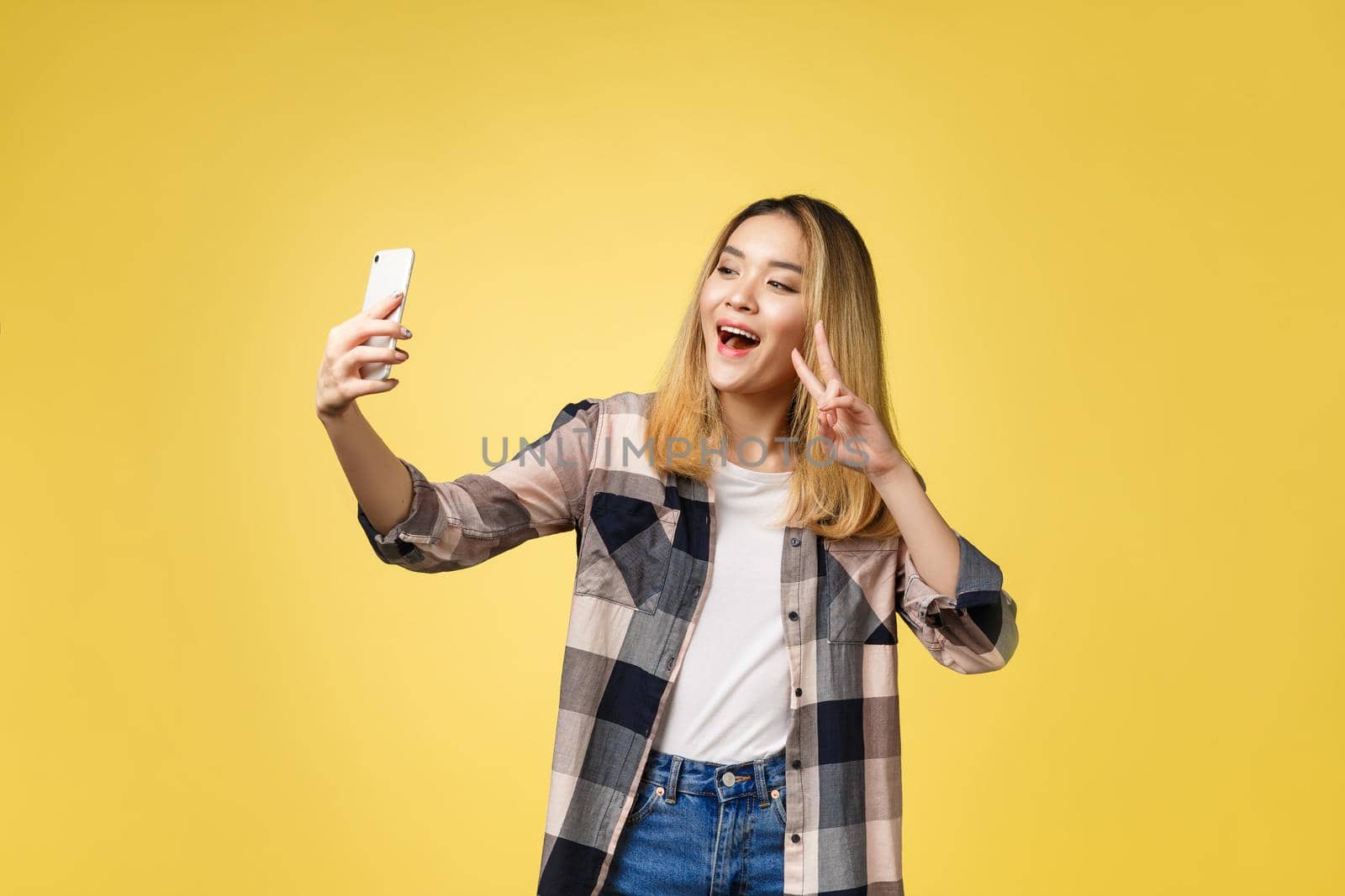 Pretty girl take a self portrait with her smart phone. Asian girl selfie, isolated on yellow background. by Benzoix