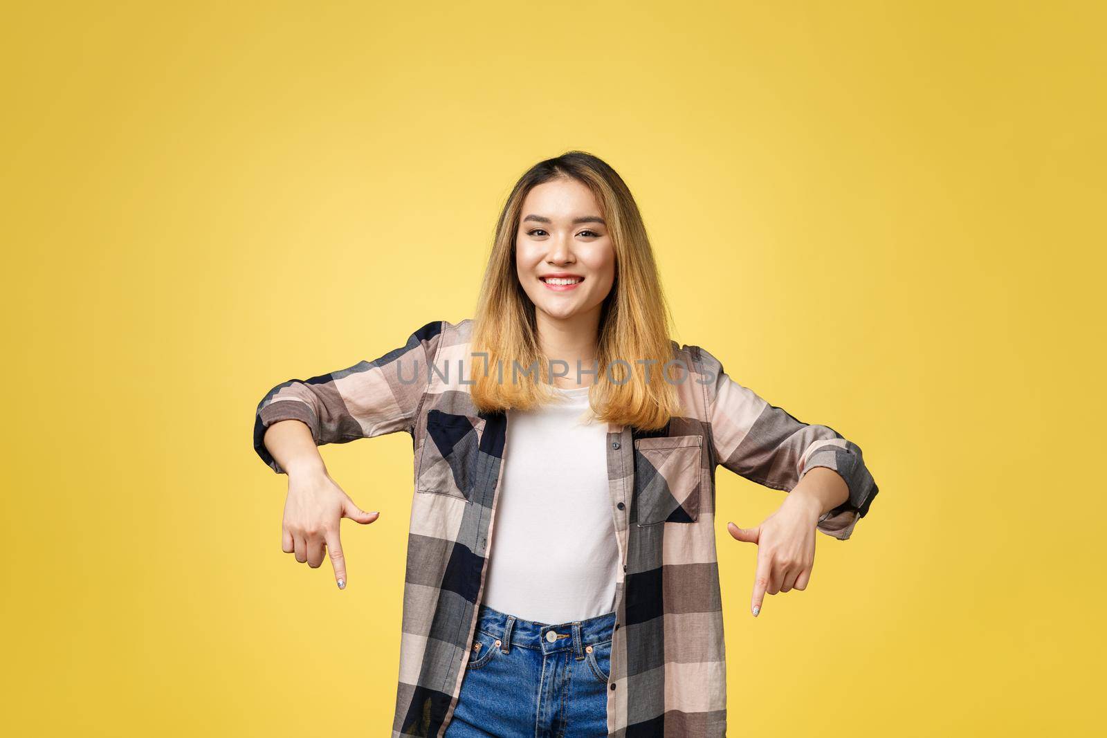 Smiling woman pointing finger side. Isolated portrait on yellow