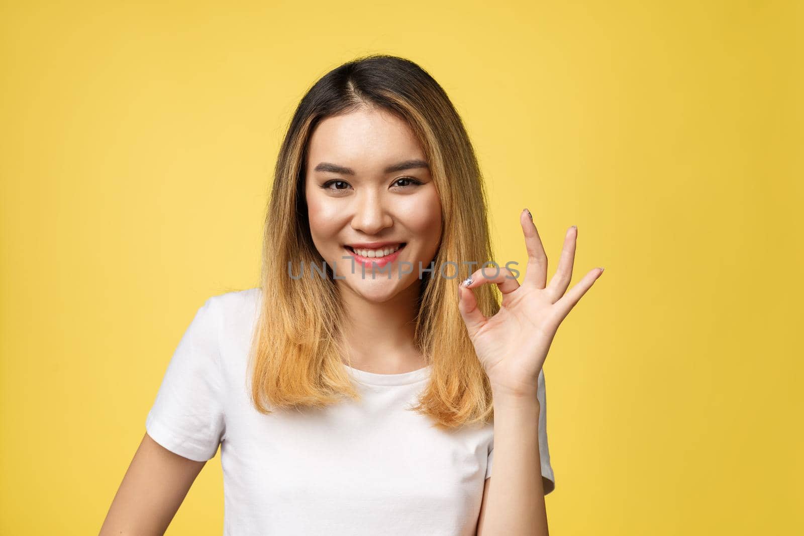 Asian young woman with ok sign gesture isolate over yellow background. by Benzoix