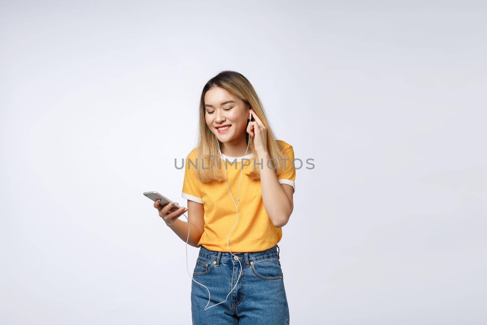 Portrait of a joyful satisfied asian woman in headphones listening to music and jumping isolated over white background.