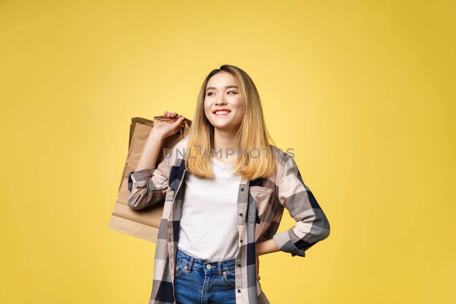 Image of happy emotional young asian woman isolated over yellow background with shopping bags.