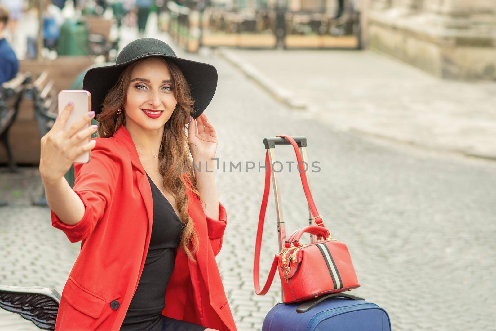 Stylish young woman is taking selfie walking on the street of old European city.