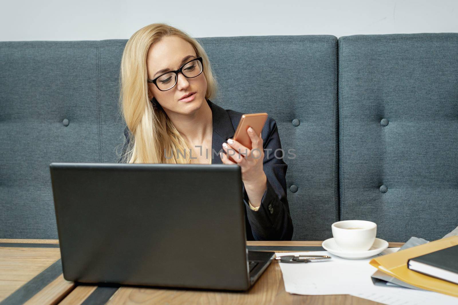 Young woman is using smartphone sitting at wooden table in coffee shop.