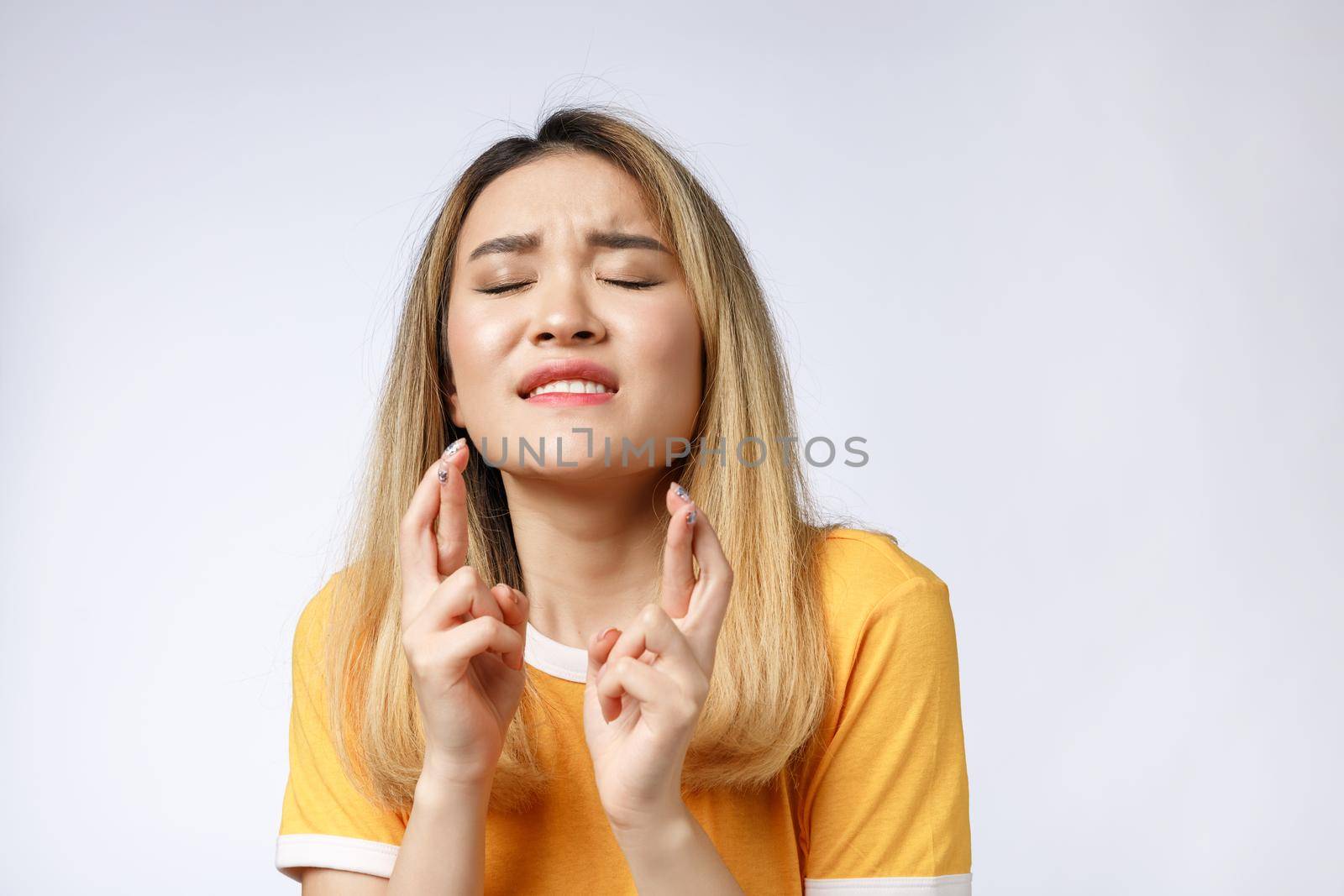 Portrait of praying young woman wearing casual clothing begging god please looking up with keeping fingers crossed isolated over gray background