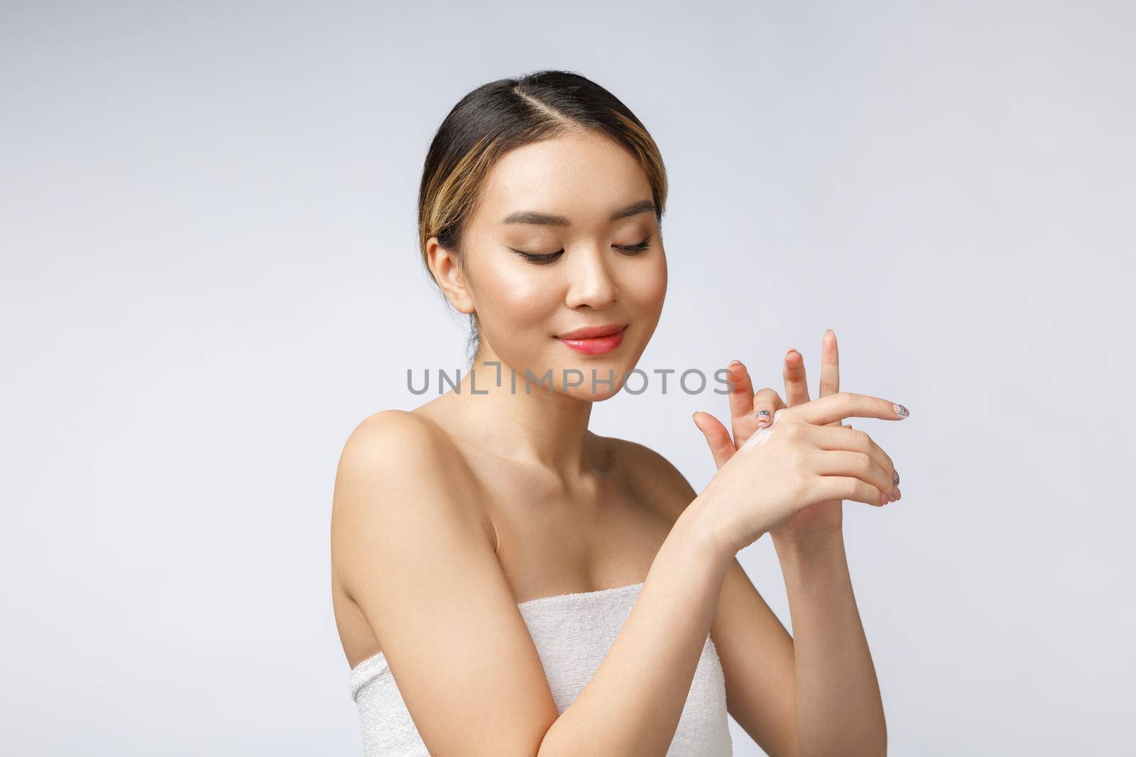 Asian woman applying cosmetic cream on skin on isolated white background.