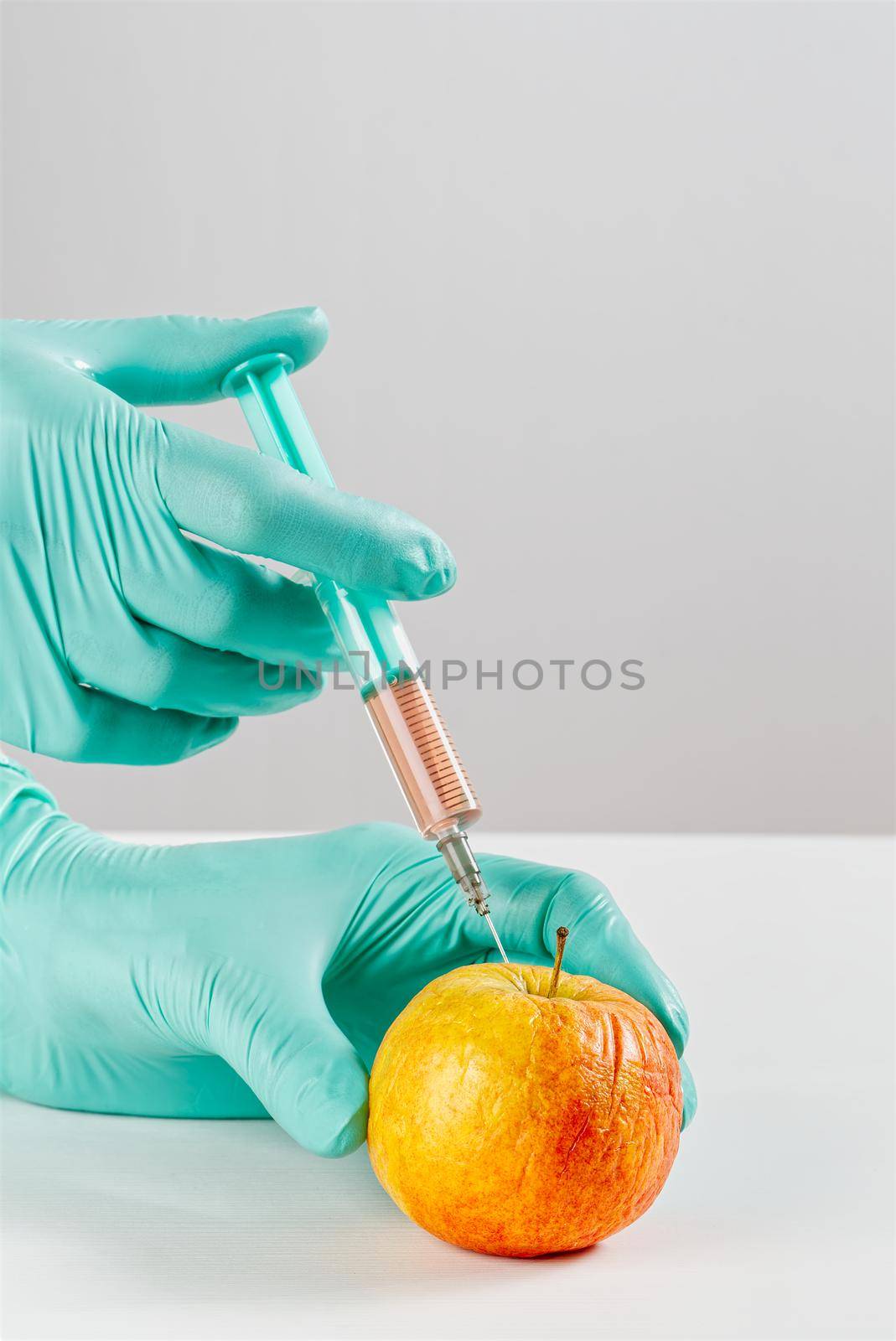 A hand in a medical glove inserts a syringe into apple. Harmful food additives. GMOs Concept. Injecting on apple at laboratory. Fruit genetic modification concept.
