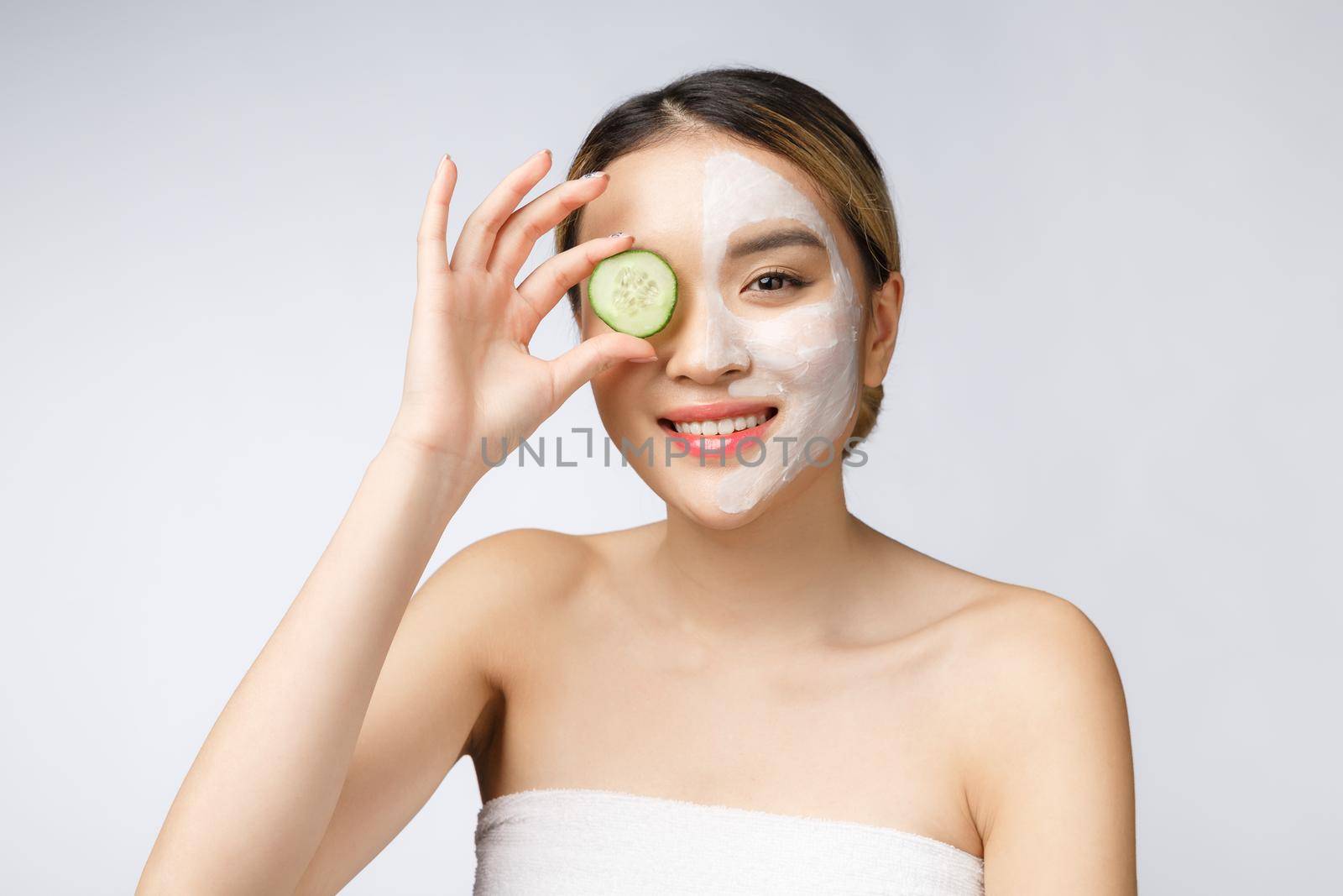 Asian young beautiful smiling woman with flawless complexion holding cucumber slices over eye