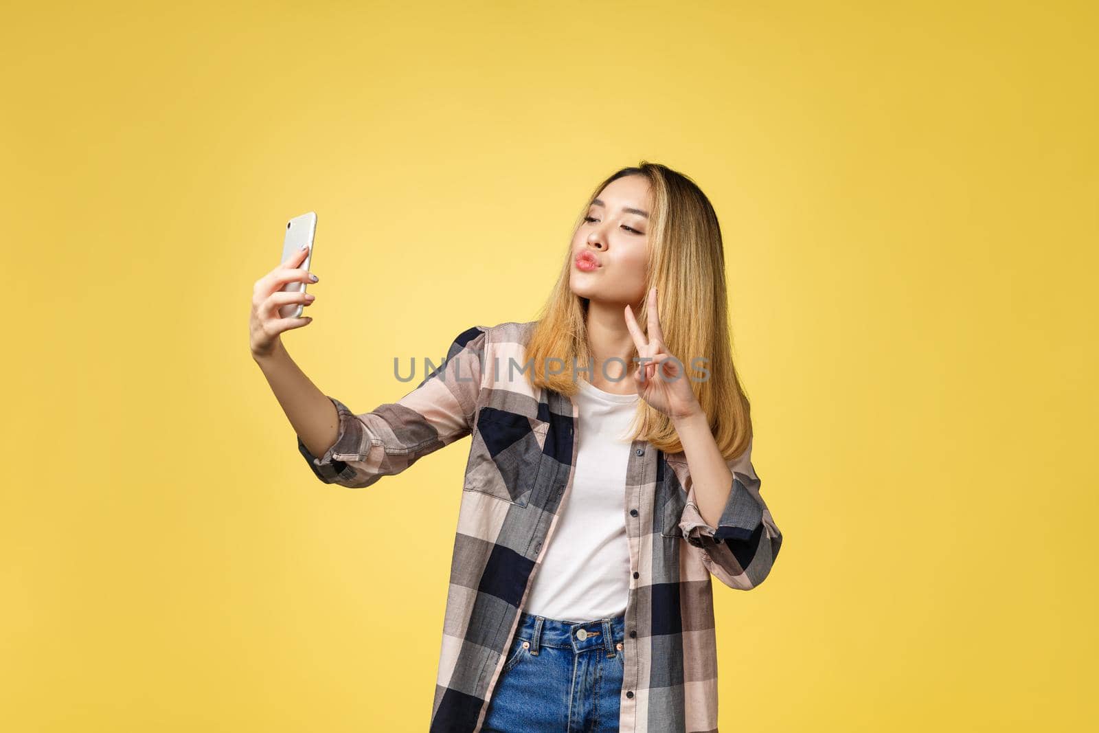 Pretty girl take a self portrait with her smart phone. Asian girl selfie, isolated on yellow background