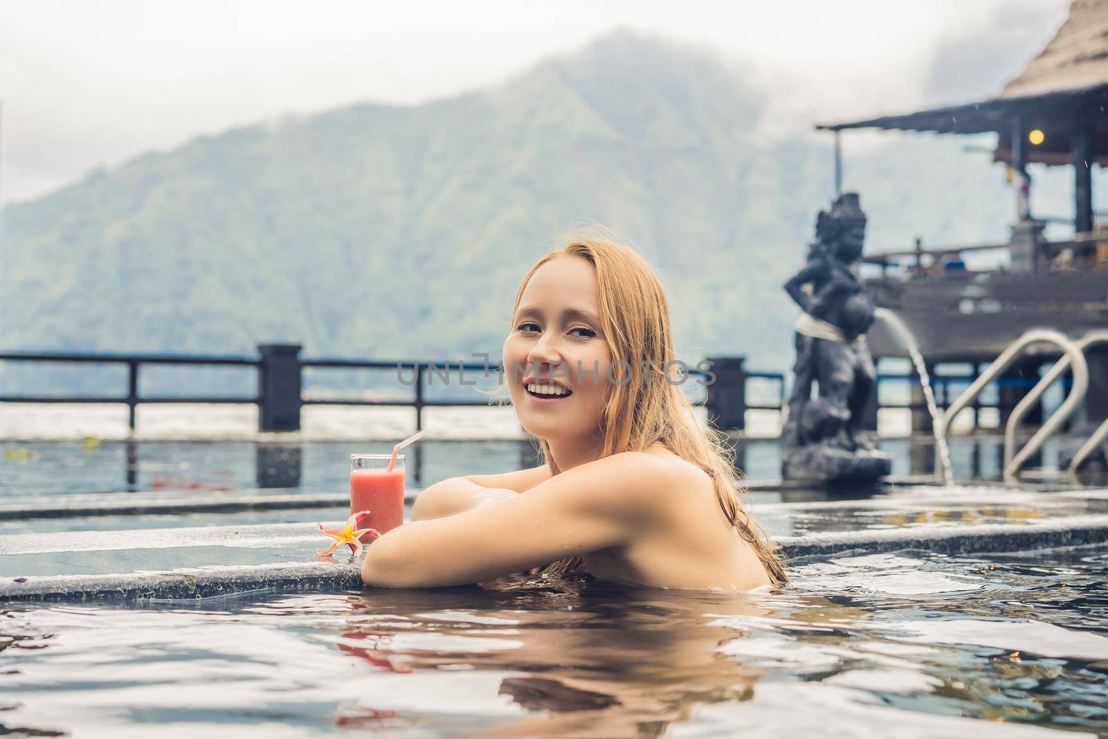 Geothermal spa. Woman relaxing in hot spring pool against the lake. hot springs concept. Drinking guava juice.