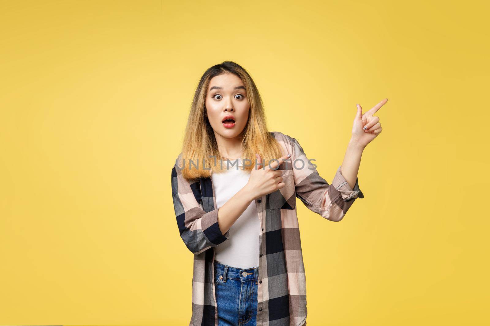 Smiling woman pointing finger side. Isolated portrait on yellow