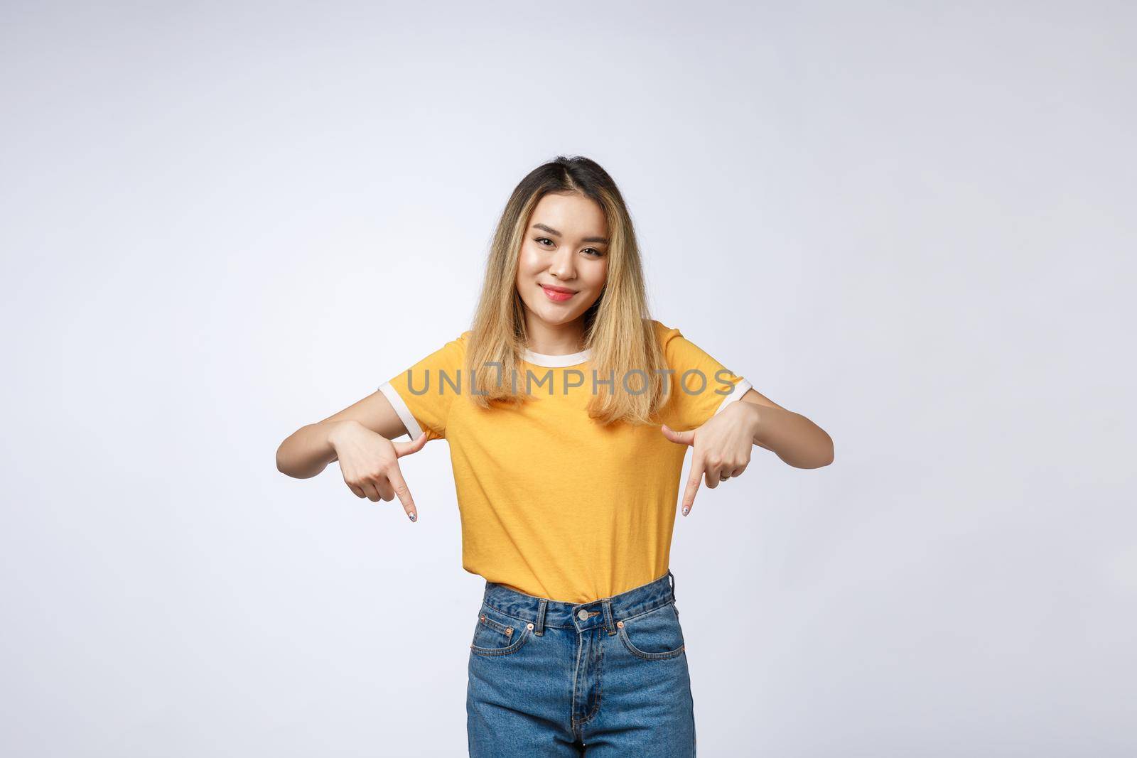 Beautiful young Asian woman point down to blank space on grey background