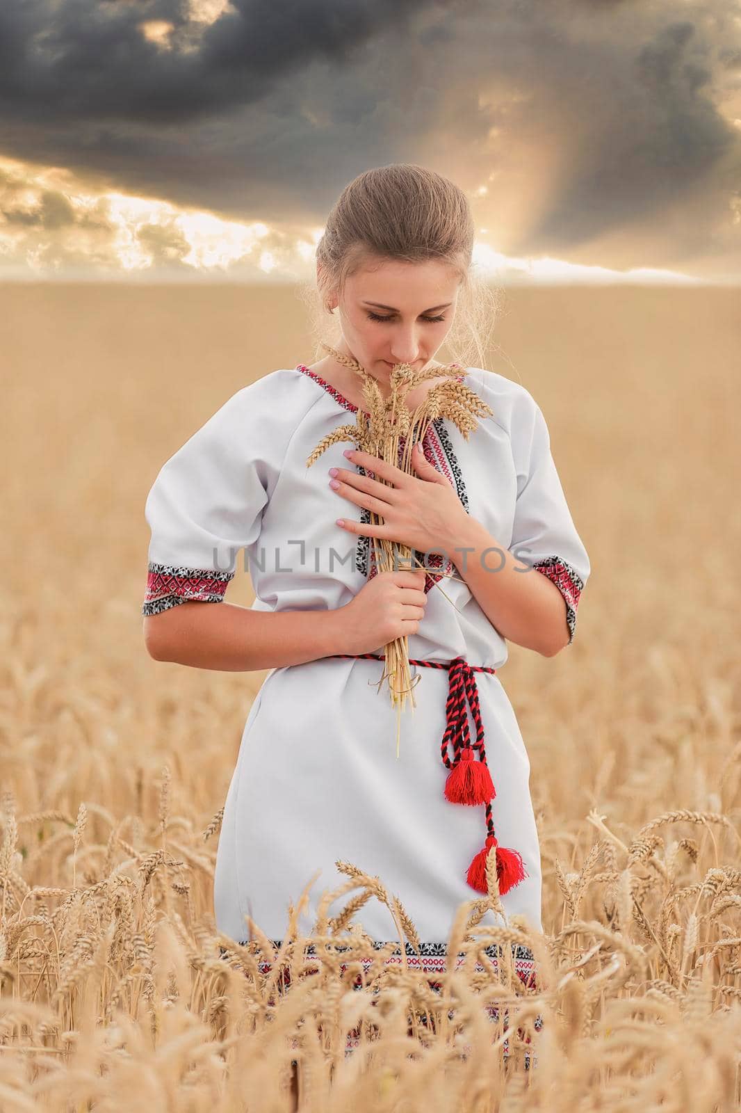 girl in an embroidered shirt on a wheat field and a sunset sky