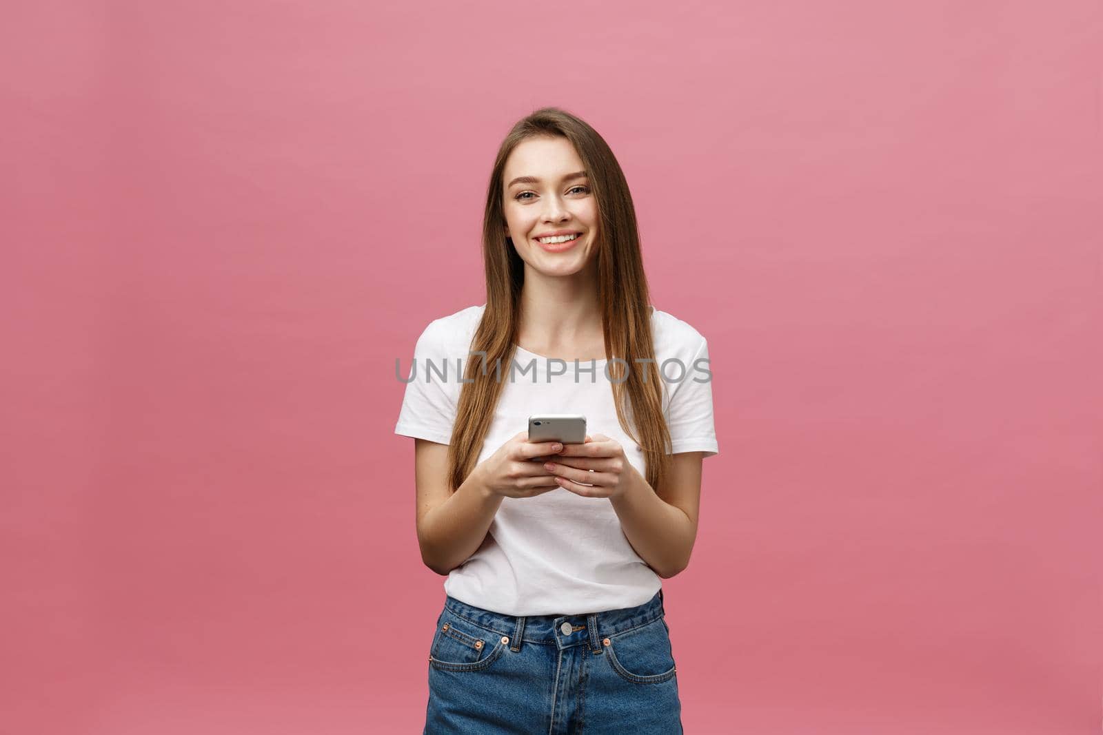 Photo of cheerful cute beautiful young woman chatting by mobile phone isolated over pink wall background