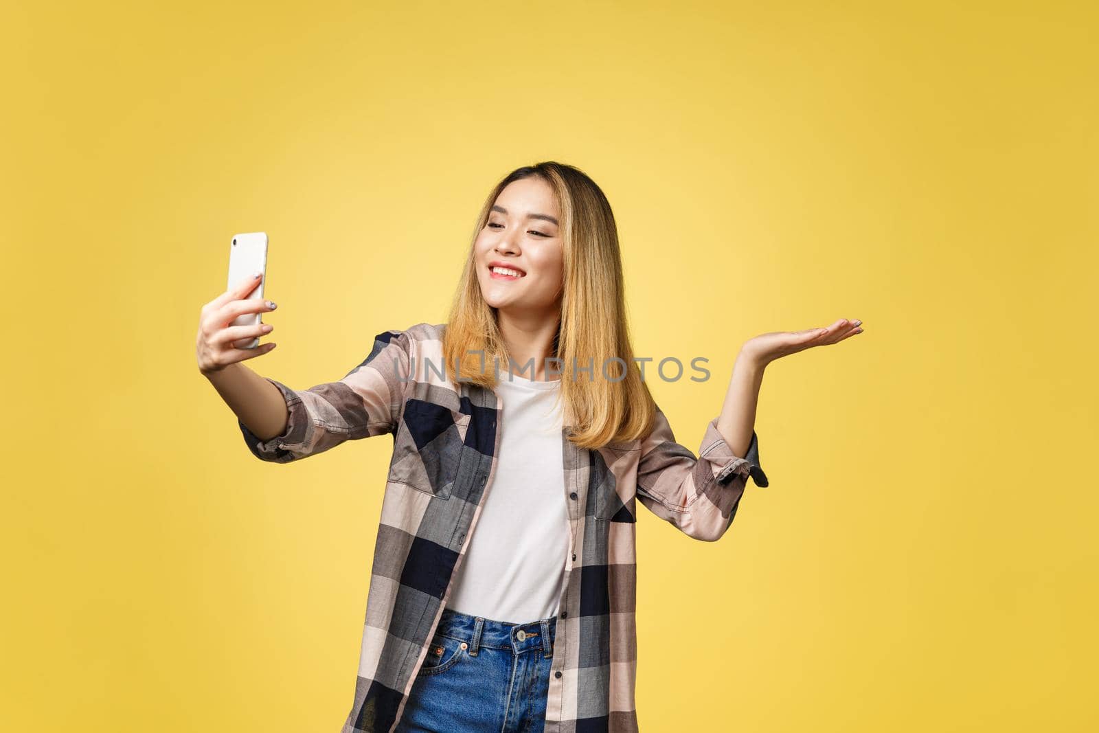 Pretty girl take a self portrait with her smart phone. Asian girl selfie, isolated on yellow background