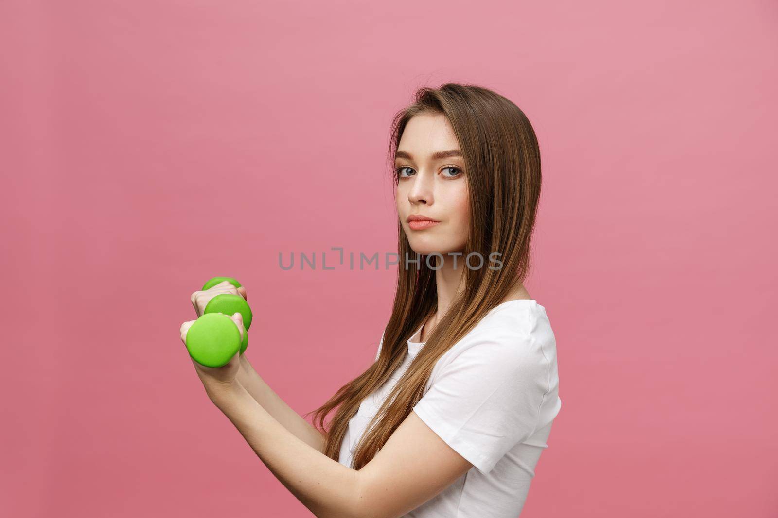 Fitness, young woman with dumbbells at studio background. Pretty girl isolate over pink.