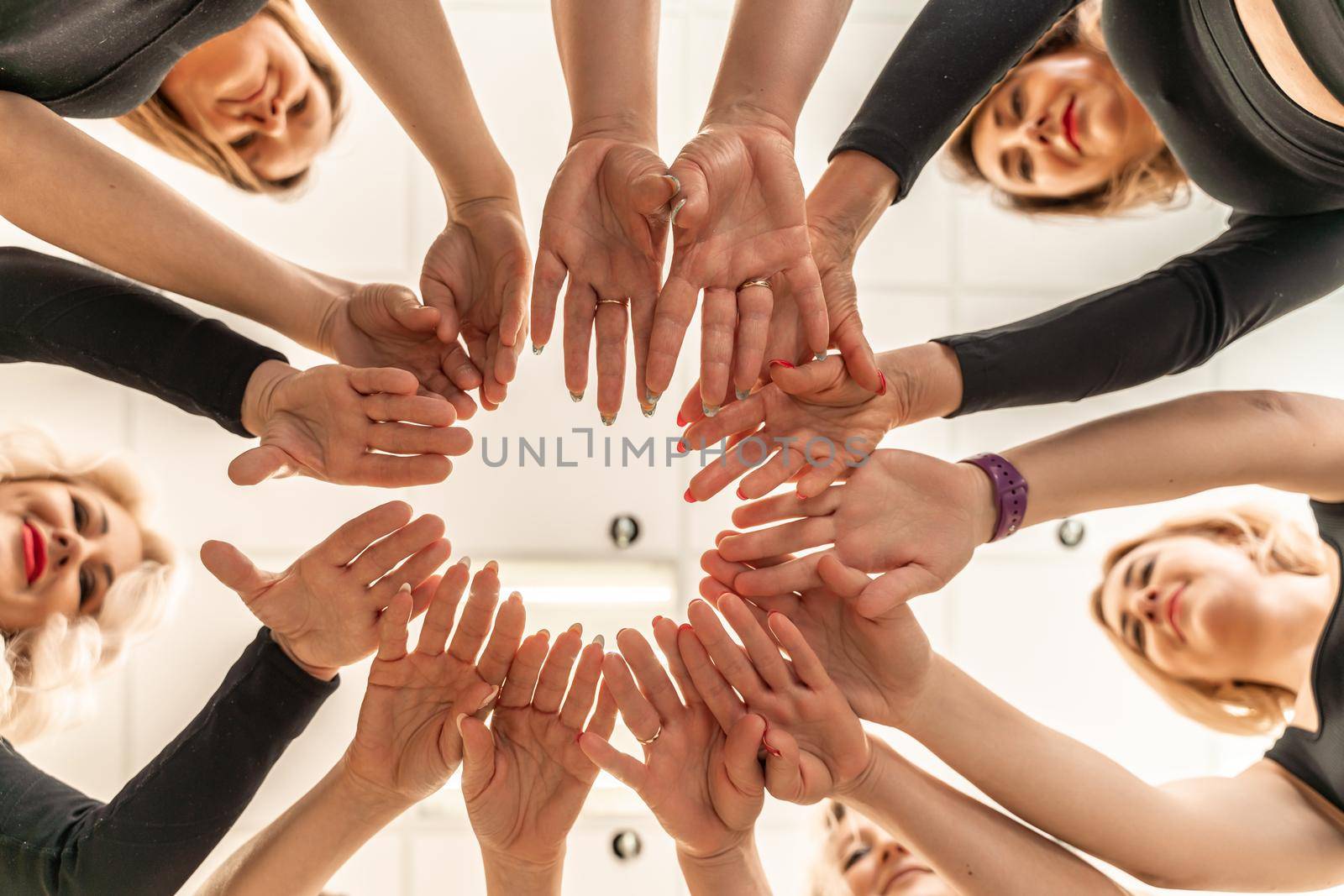 Team of people holding hands. Group of happy young women holding hands. Bottom view, low angle shot of human hands. Friendship and unity concept.