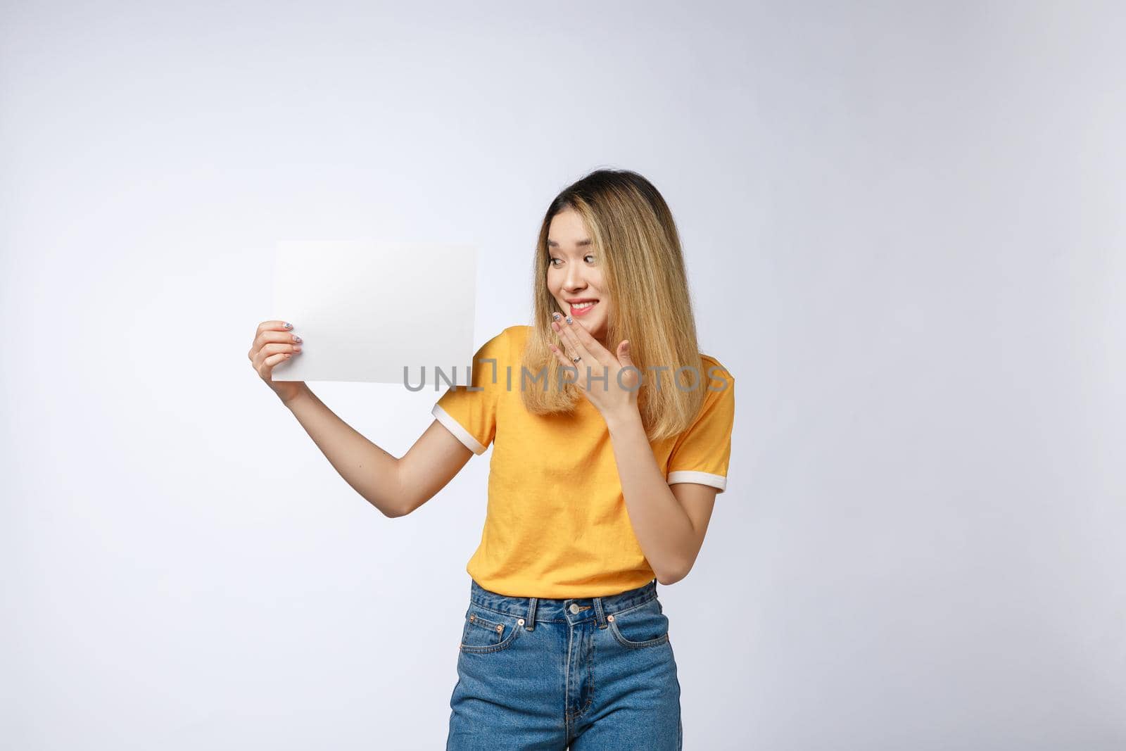 Banner sign woman peeking over edge of blank empty paper billboard with copy space for text. Beautiful Asian Caucasian woman looking surprised and scared - funny. Isolated on white background.