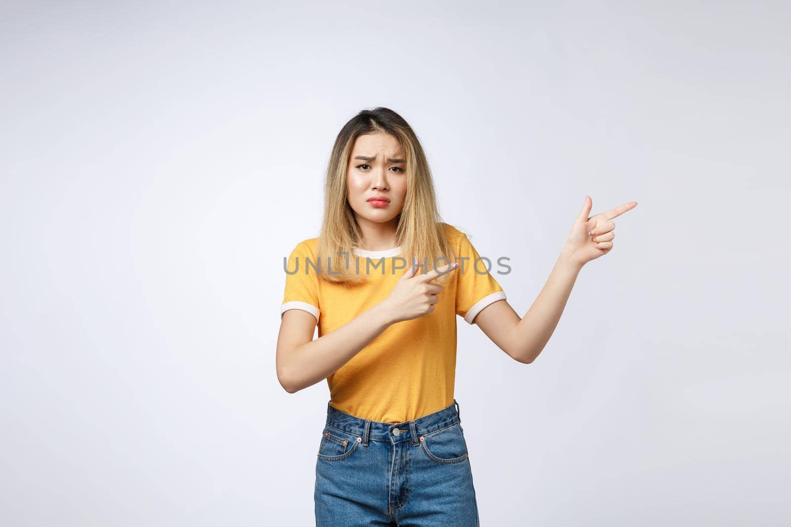 Young Asian woman looking angry and sad while pointing finger at camera isolated against white background