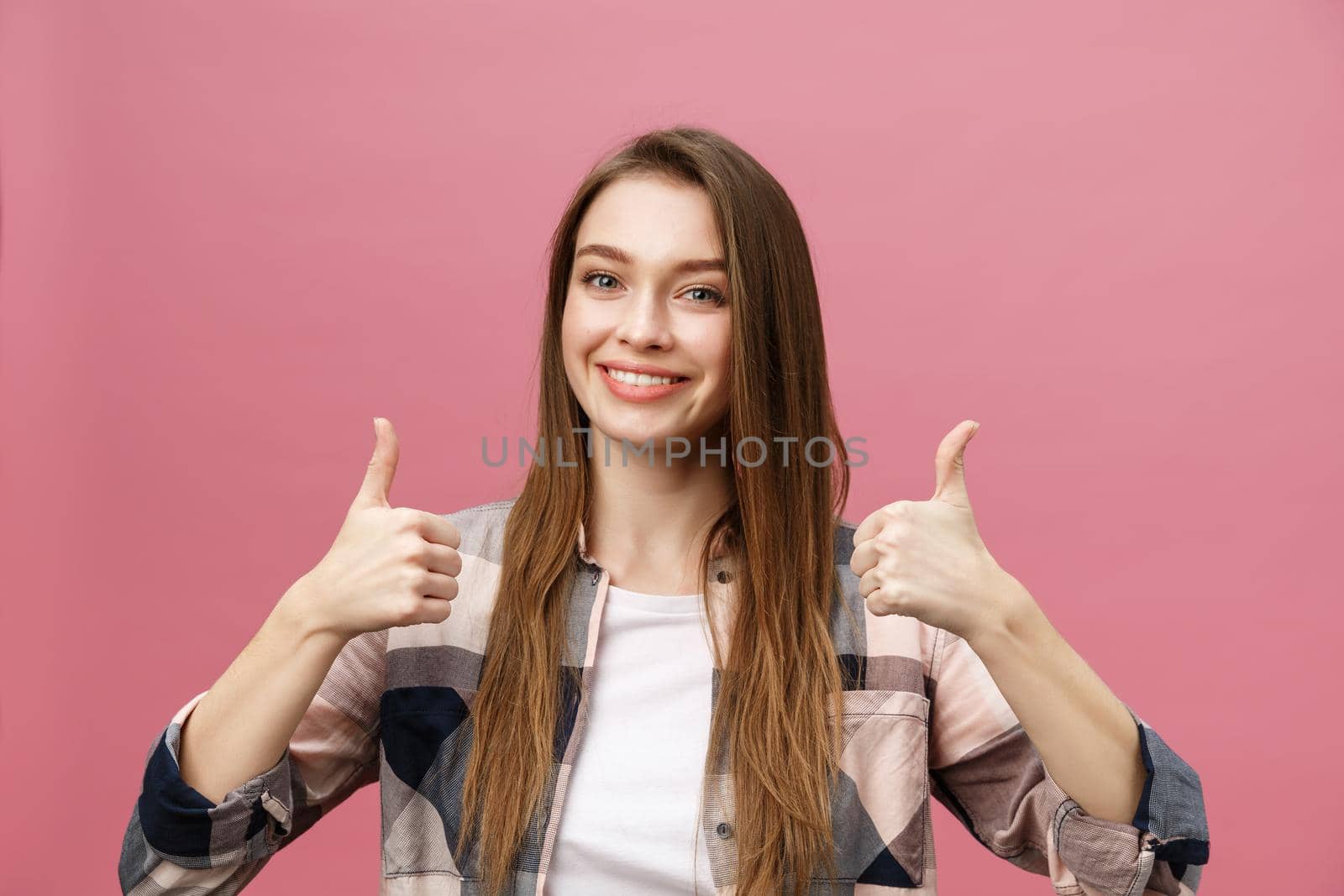 Close-up shot of smiling pretty girl showing thumb up gesture. Female isolated over pink background in the studio