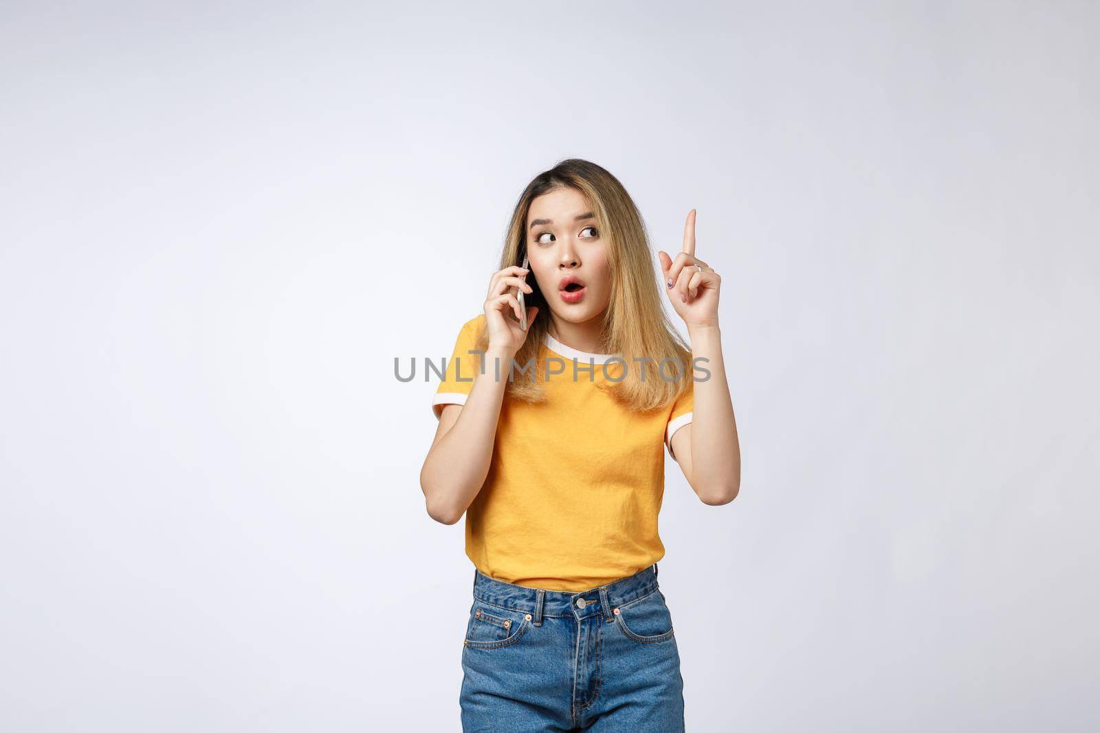 Portrait of a pensive young asian woman holding mobile phone and looking away thinking isolated over white background.