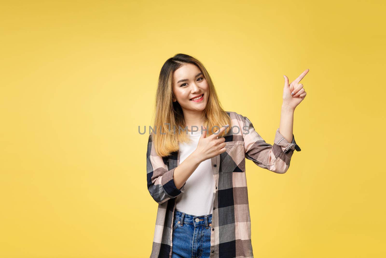 Smiling woman pointing finger side. Isolated portrait on yellow. by Benzoix