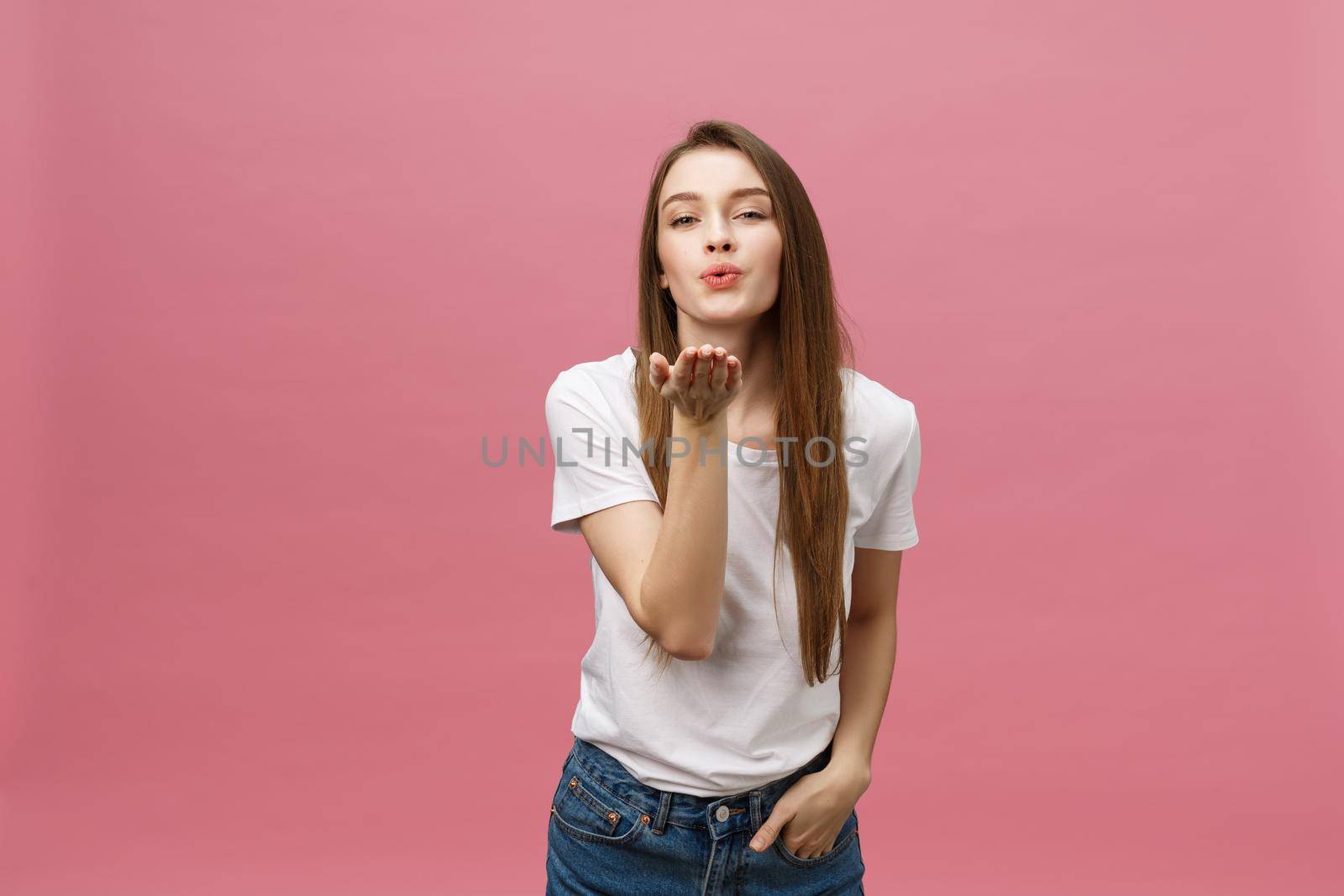 Beautiful woman with makeup and long blonde hair blows kiss, demonstrates her good feelings, says goodbye on distance, isolated over pink background.
