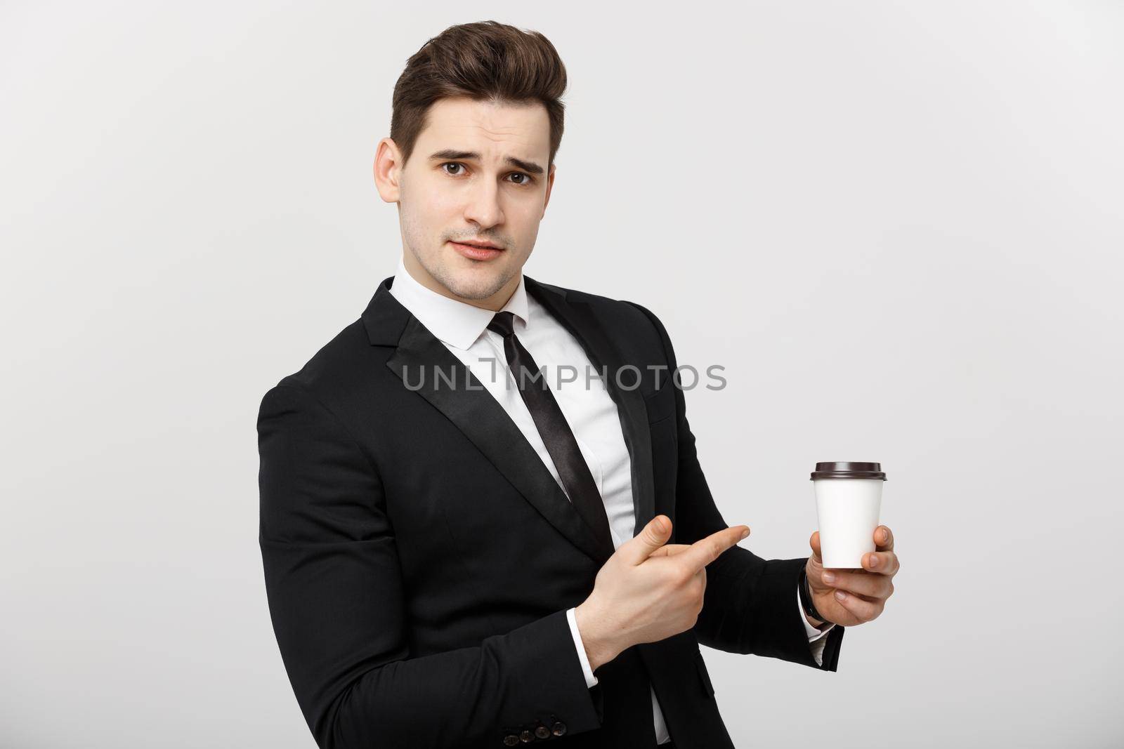 Business Concept: Half-length shot of handsome businessman in a suit holding a cup of coffee and pointing at it with his finger.