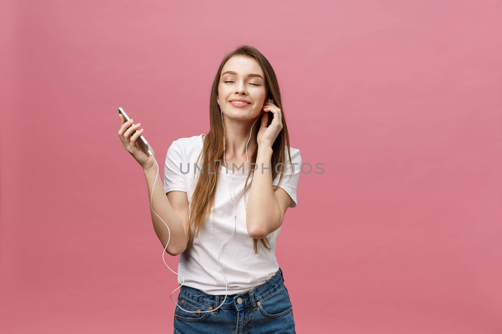 Lifestyle Concept. Young woman using phone for listening to music on pink background.