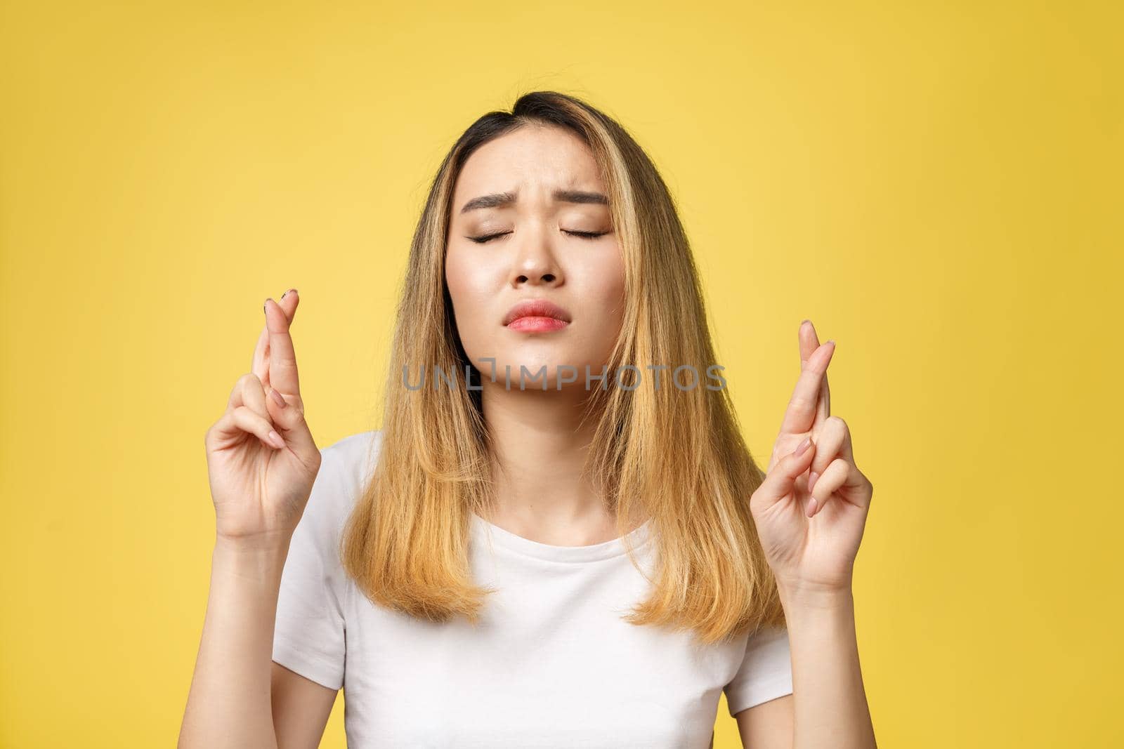 Young happy asian woman with fingers crossed on yellow background.