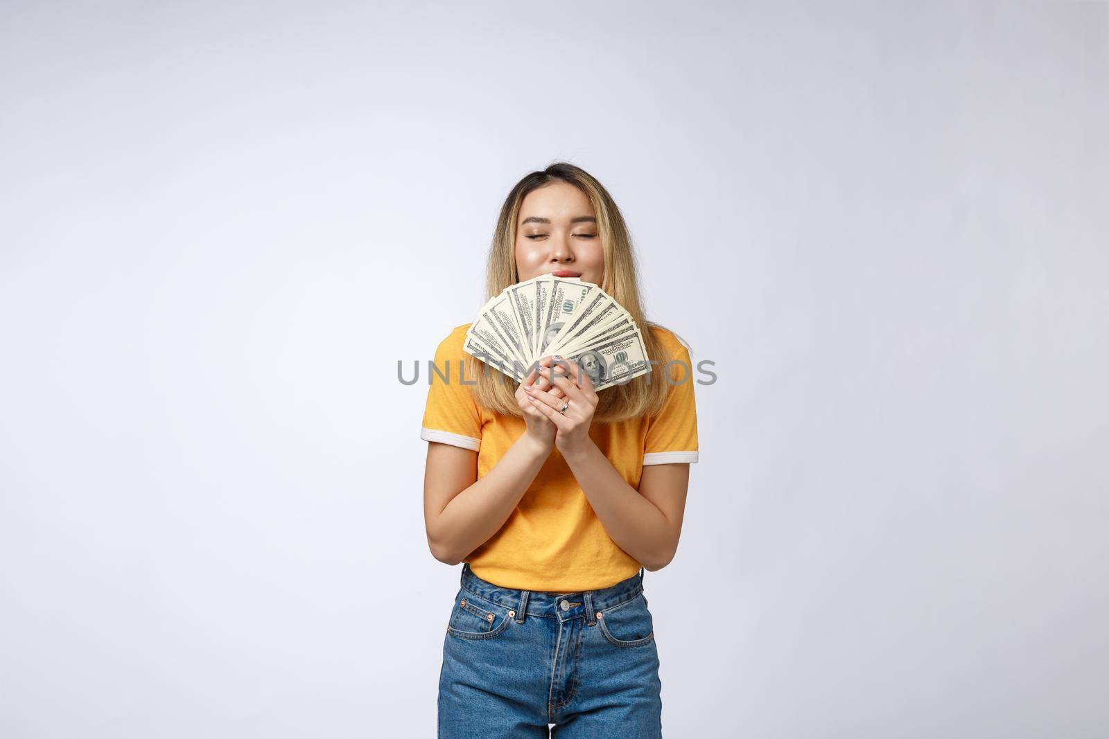 Asian woman holding cash notes isolated in white background. Young asian woman in white t-shirt in winning surprise, holding dollar note. Young rich hipster concept. by Benzoix