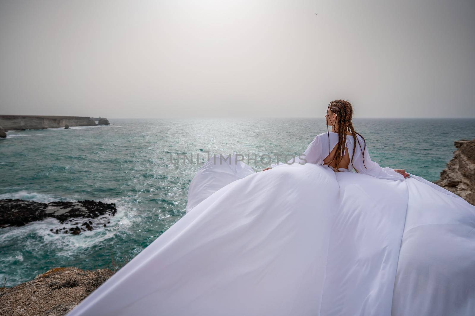 Happy freedom woman on the beach enjoying and posing in white dress. Rear view of a girl in a fluttering white dress in the wind. Holidays, holidays at sea. by Matiunina