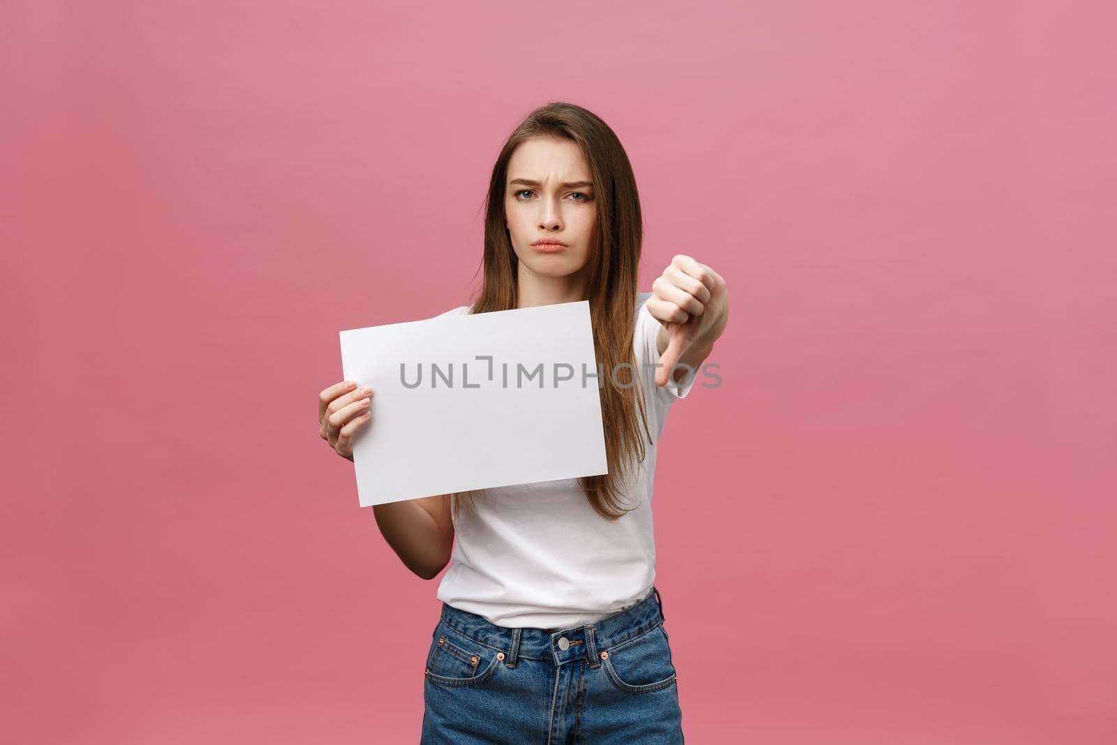 Unhappy woman giving thumbs down gesture with blank paper and negative expression and disapproval