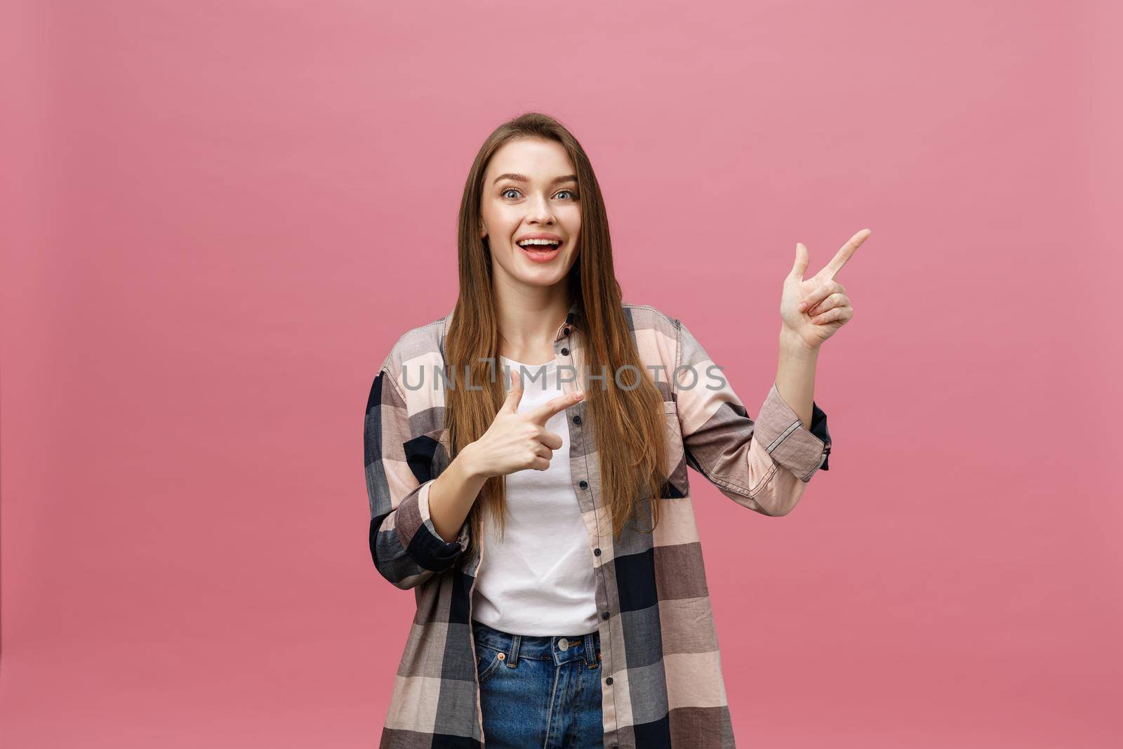 Cute young woman points a finger away isolate over pink background. Copy Space