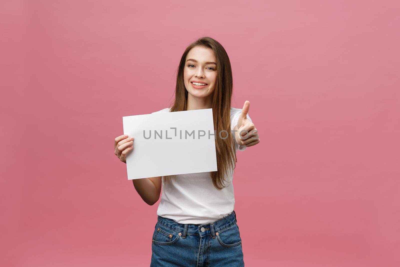 Young beauty woman hold blank card and showing thumbs up over pink background.