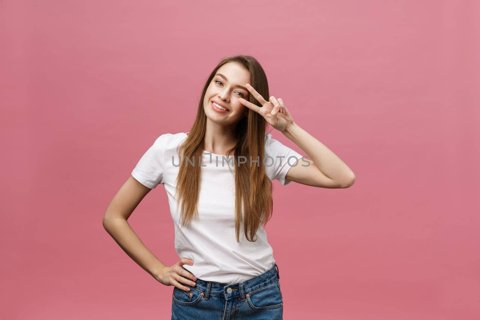 Portrait of a cheerful trendy woman showing two fingers sign over pink background.