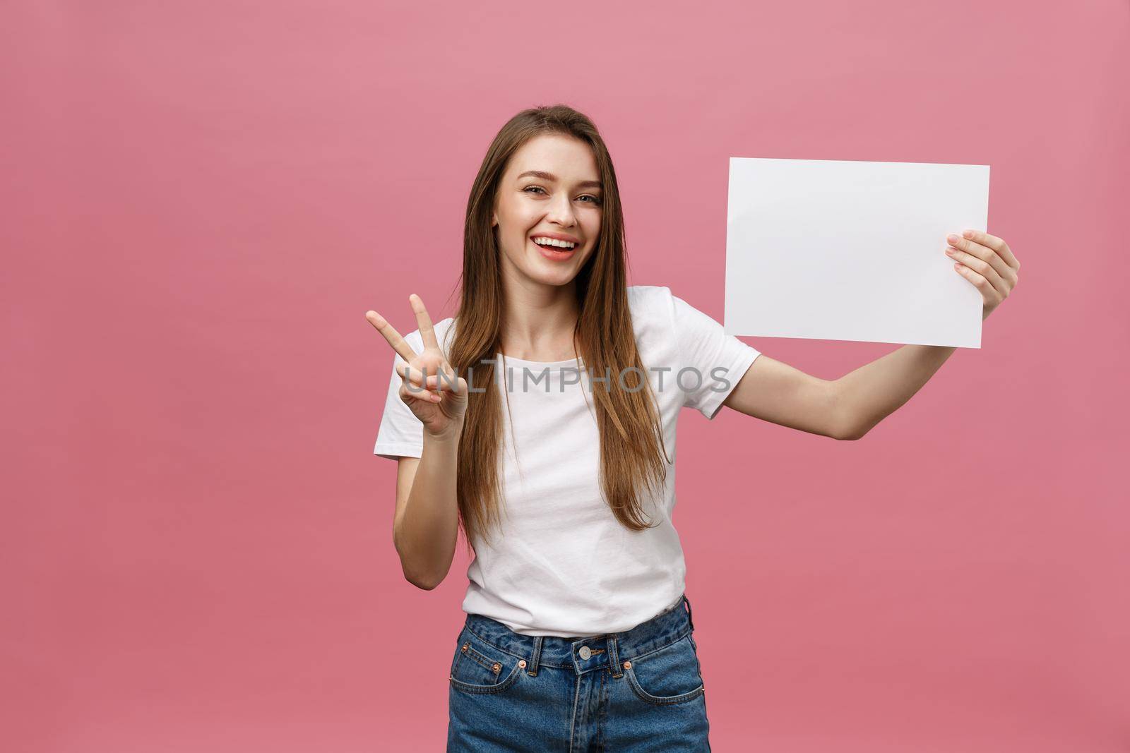 Close up portrait of positive laughing woman smiling and holding white big mockup poster isolated on pink background.