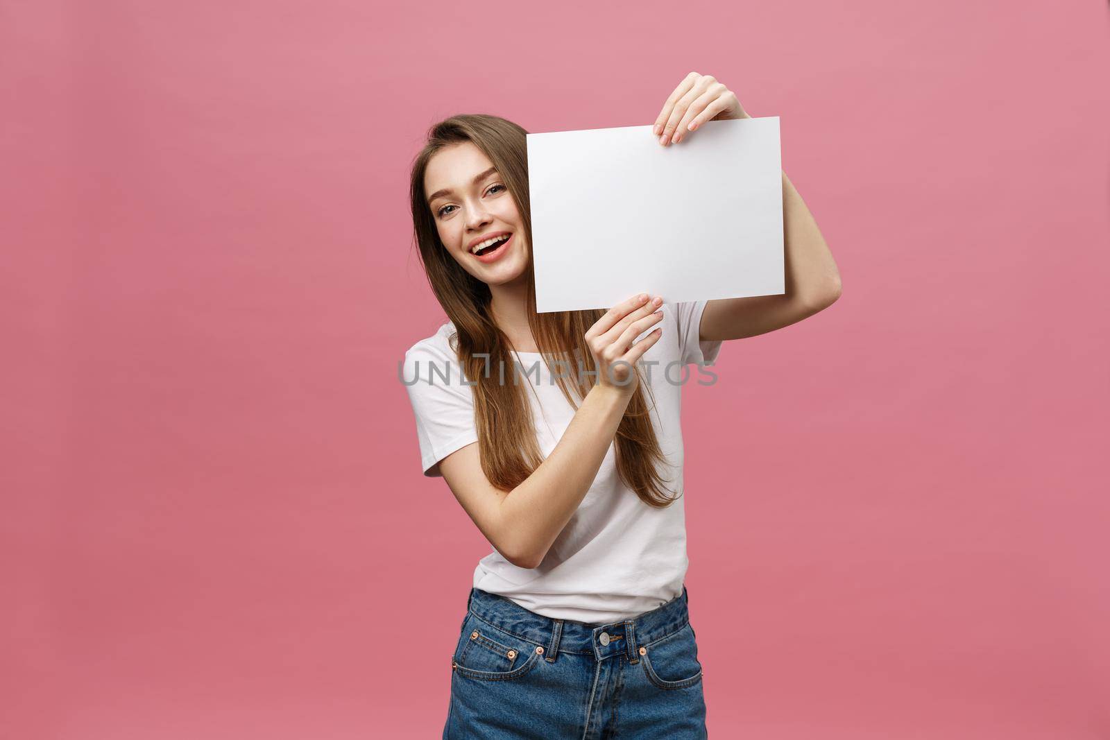 Close up portrait of positive laughing woman smiling and holding white big mockup poster isolated on pink background.