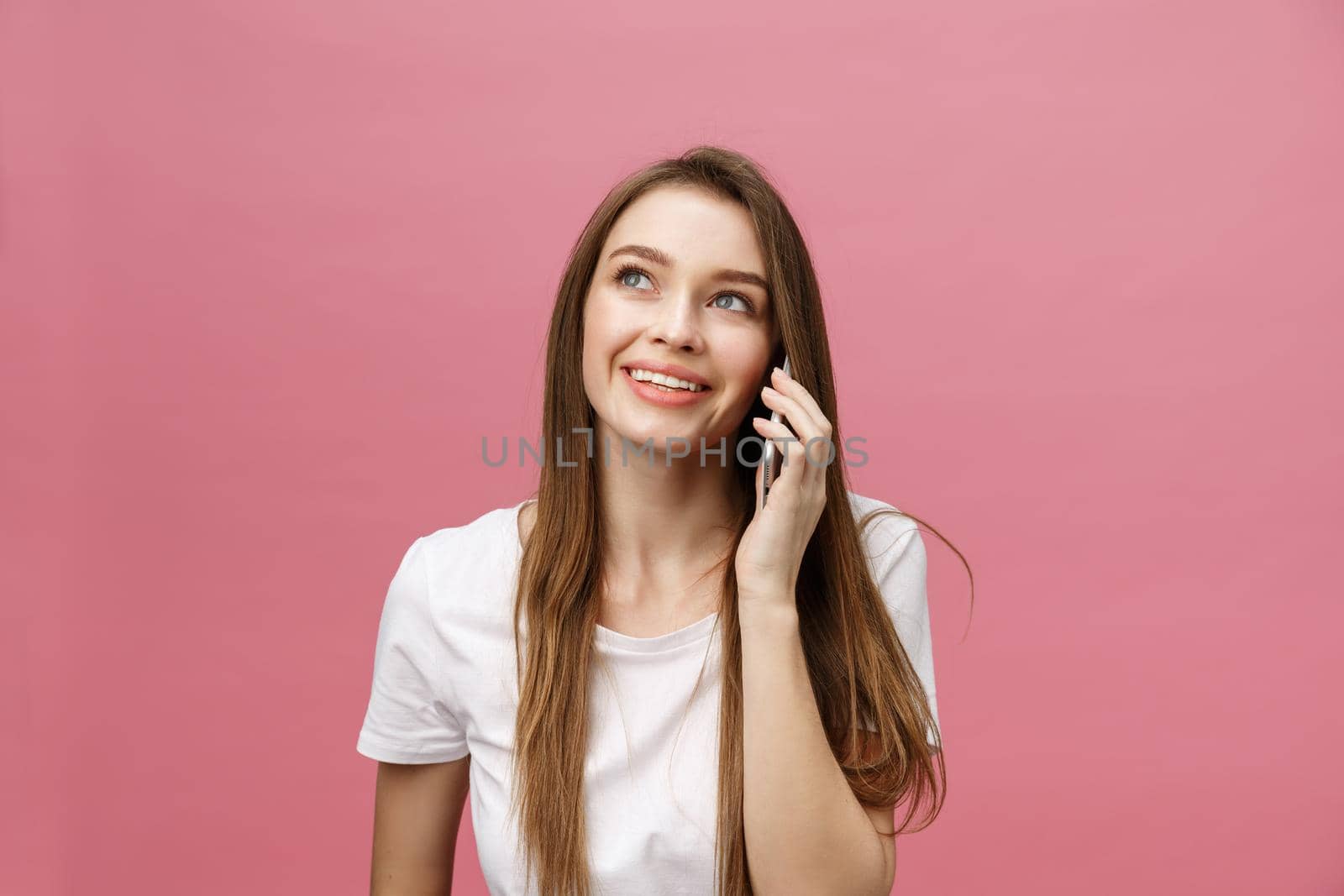 Cheerful young woman talking on mobile phone isolated on pink background.