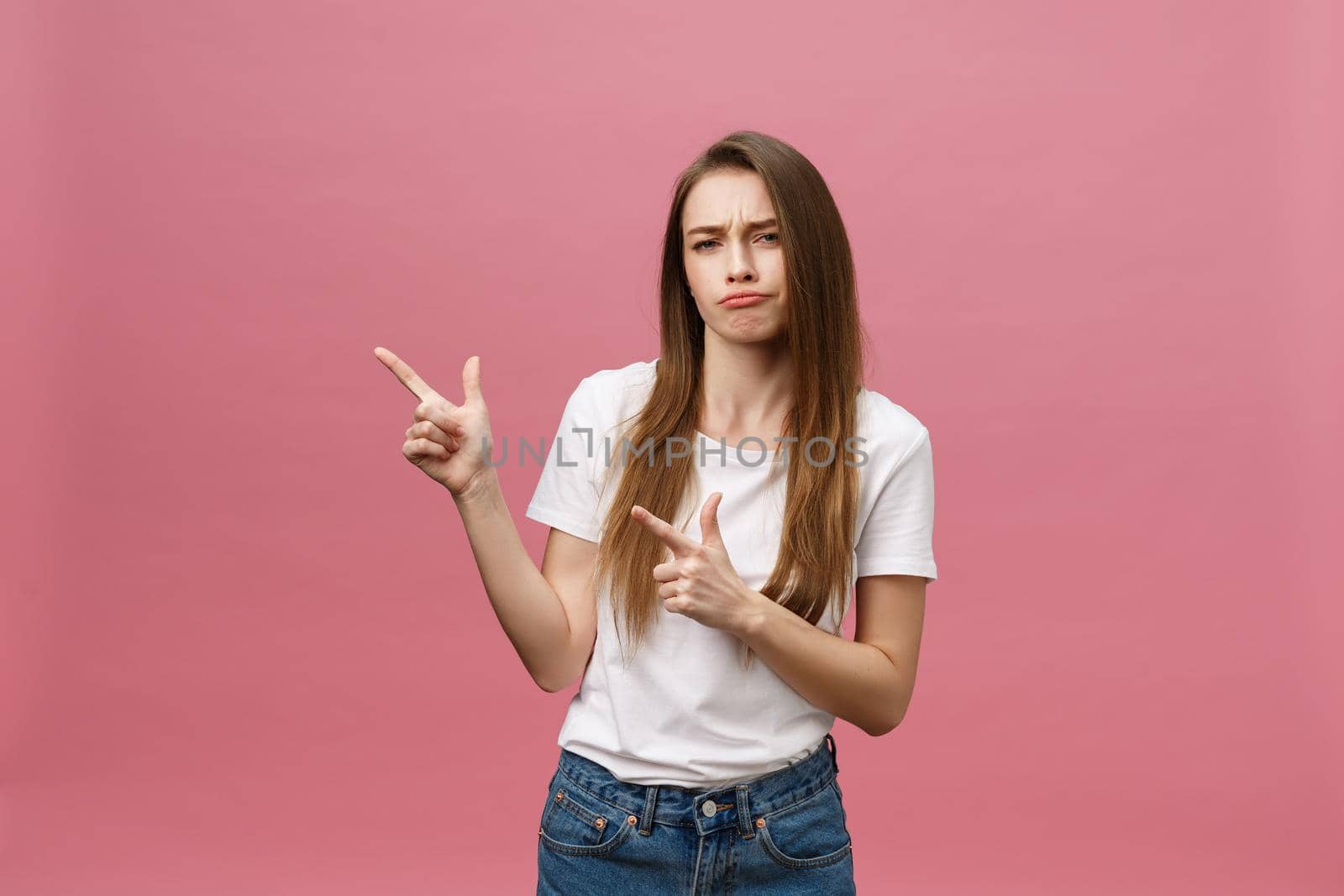 Closeup of serious strict young woman wears white shirt looks stressed and pointing up with finger isolated over pink background by Benzoix
