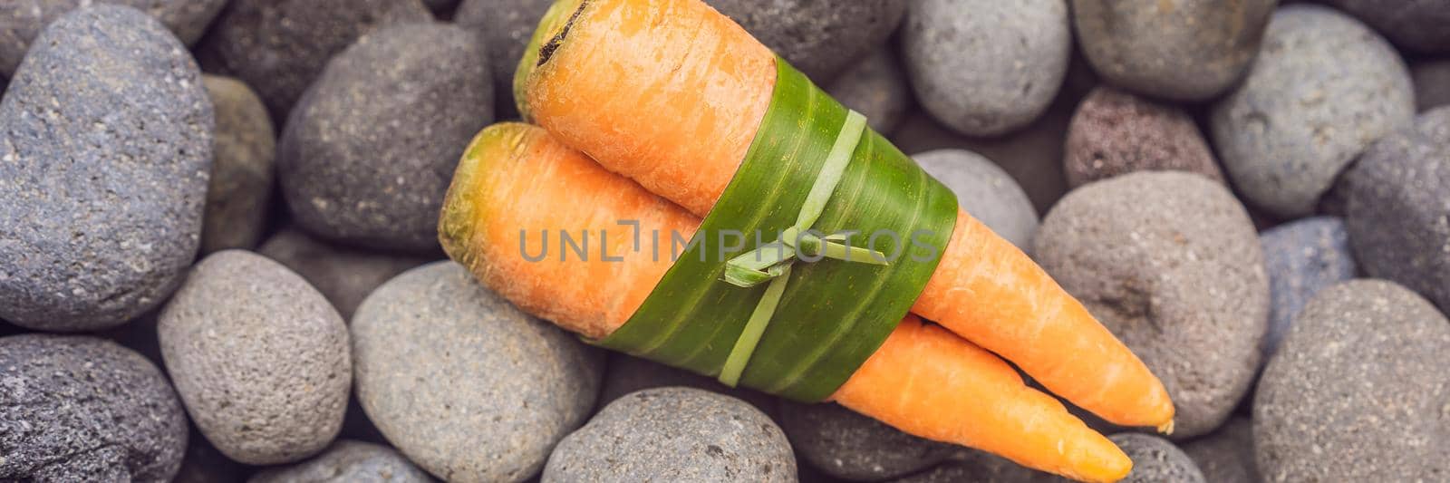 Eco-friendly product packaging concept. Carrot wrapped in a banana leaf, as an alternative to a plastic bag. Zero waste concept. Alternative packaging BANNER, LONG FORMAT by galitskaya
