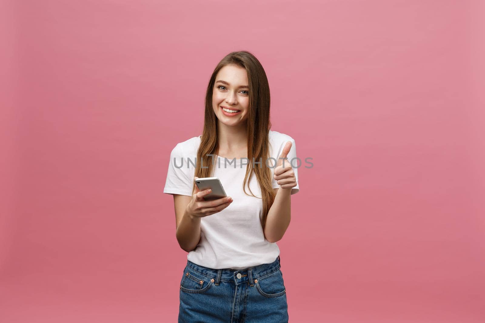 Photo of cheerful cute beautiful young woman chatting by mobile phone isolated over pink wall background