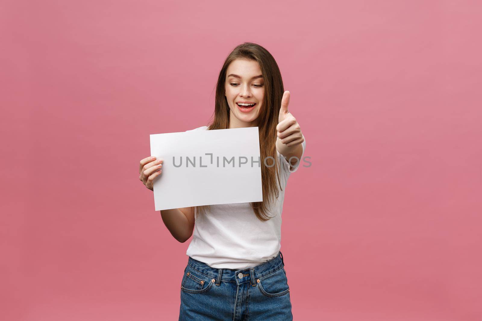 Young beauty woman hold blank card and showing thumbs up over pink background.