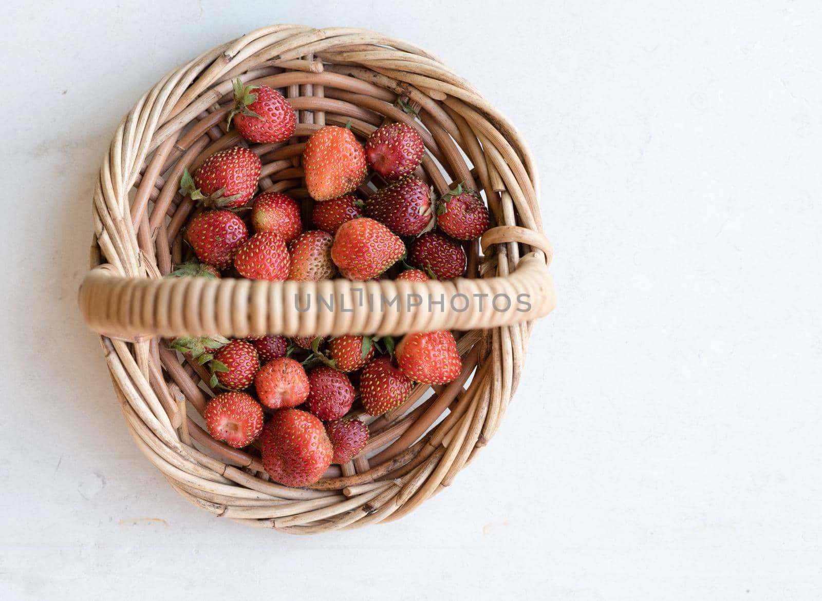 High angle view of home grown strawberries in small wicker basket on limestone background (selective focus) by natalie_board