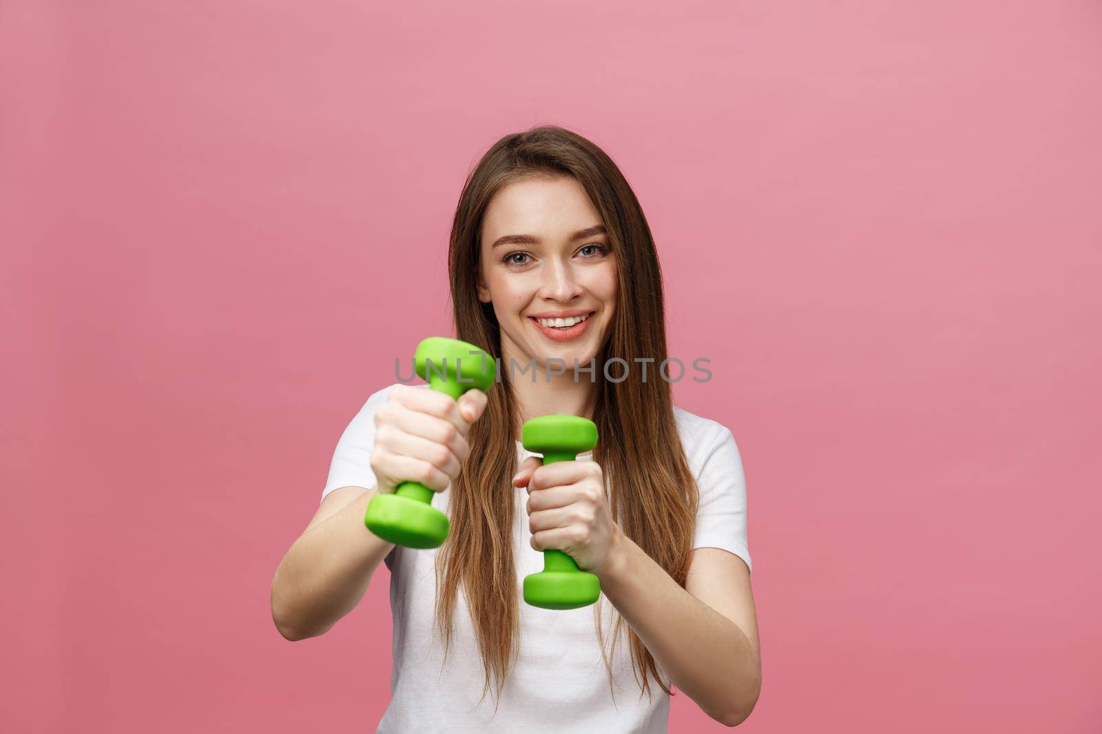 Fitness, young woman with dumbbells at studio background. Pretty girl isolate over pink.