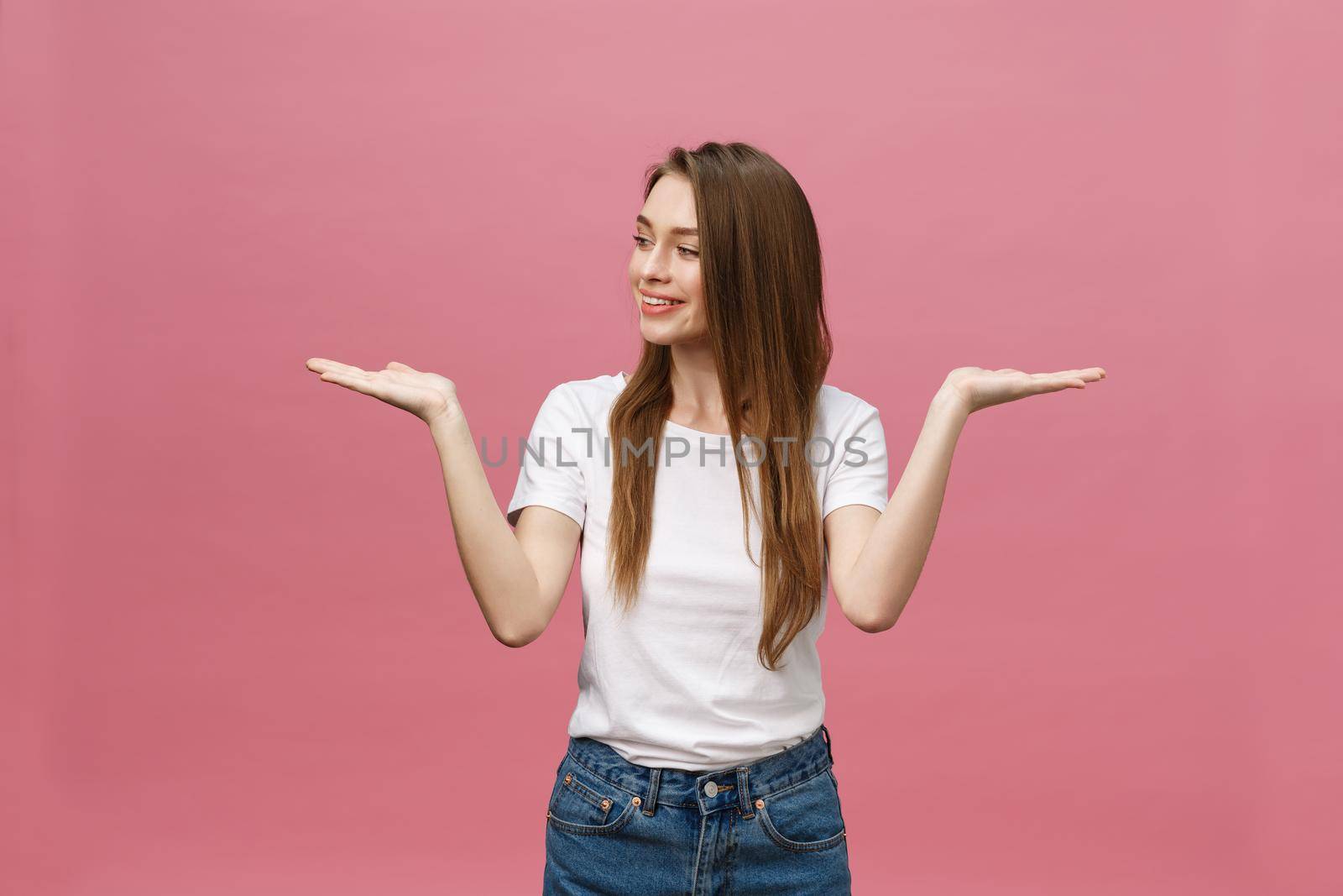 young girl with white shirt pointing hand on side to present a product on isolated pink background by Benzoix